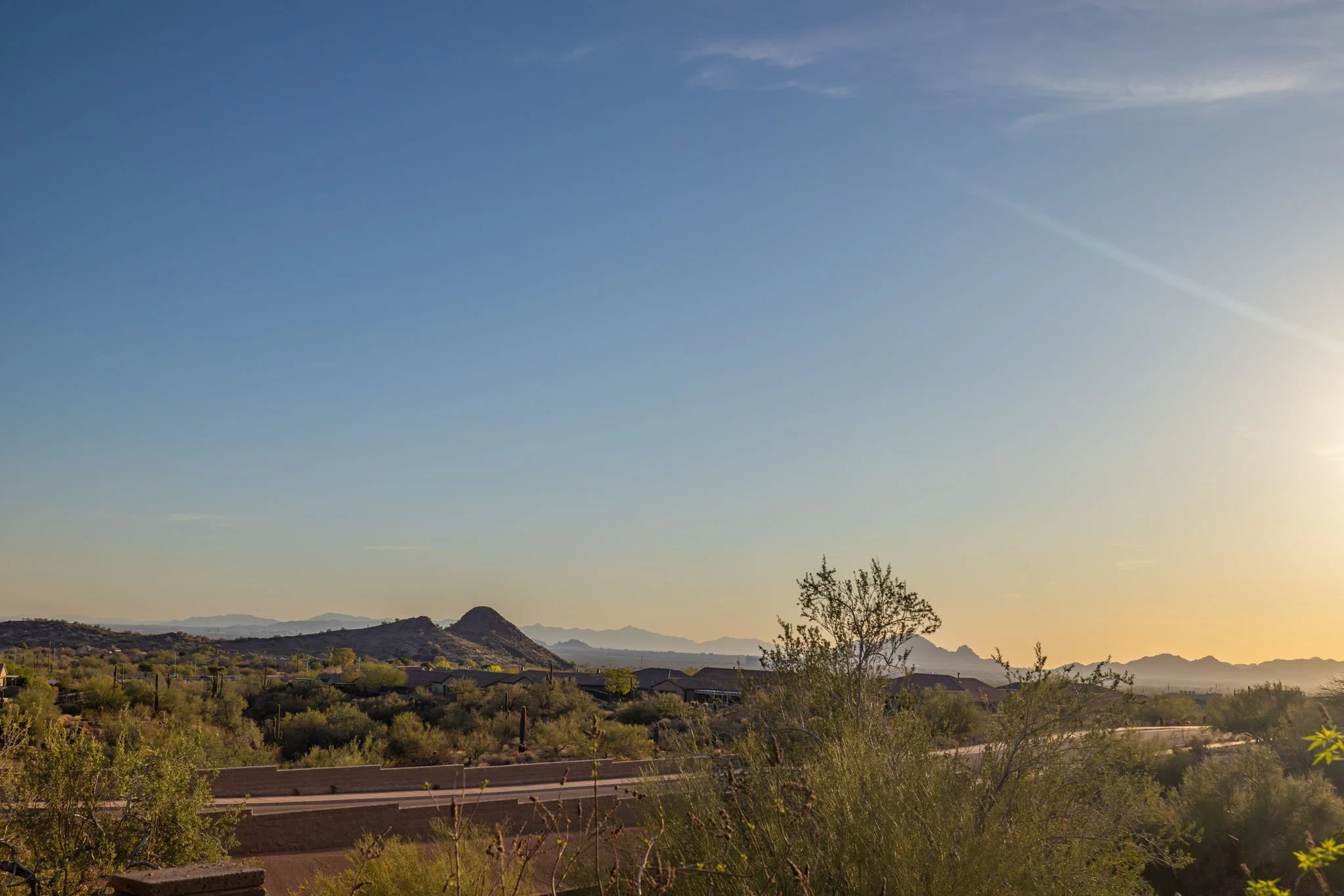 Desert landscape at sunset with mountains, shrubs, and a clear sky.