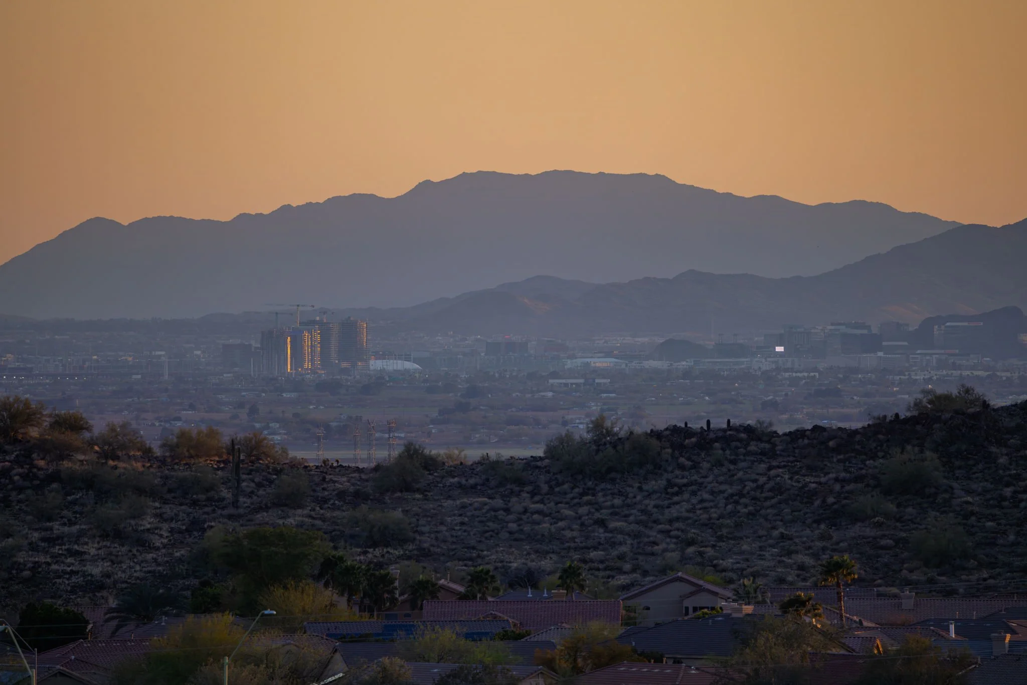 A landscape view of a city with mountains in the background during sunset or sunrise.