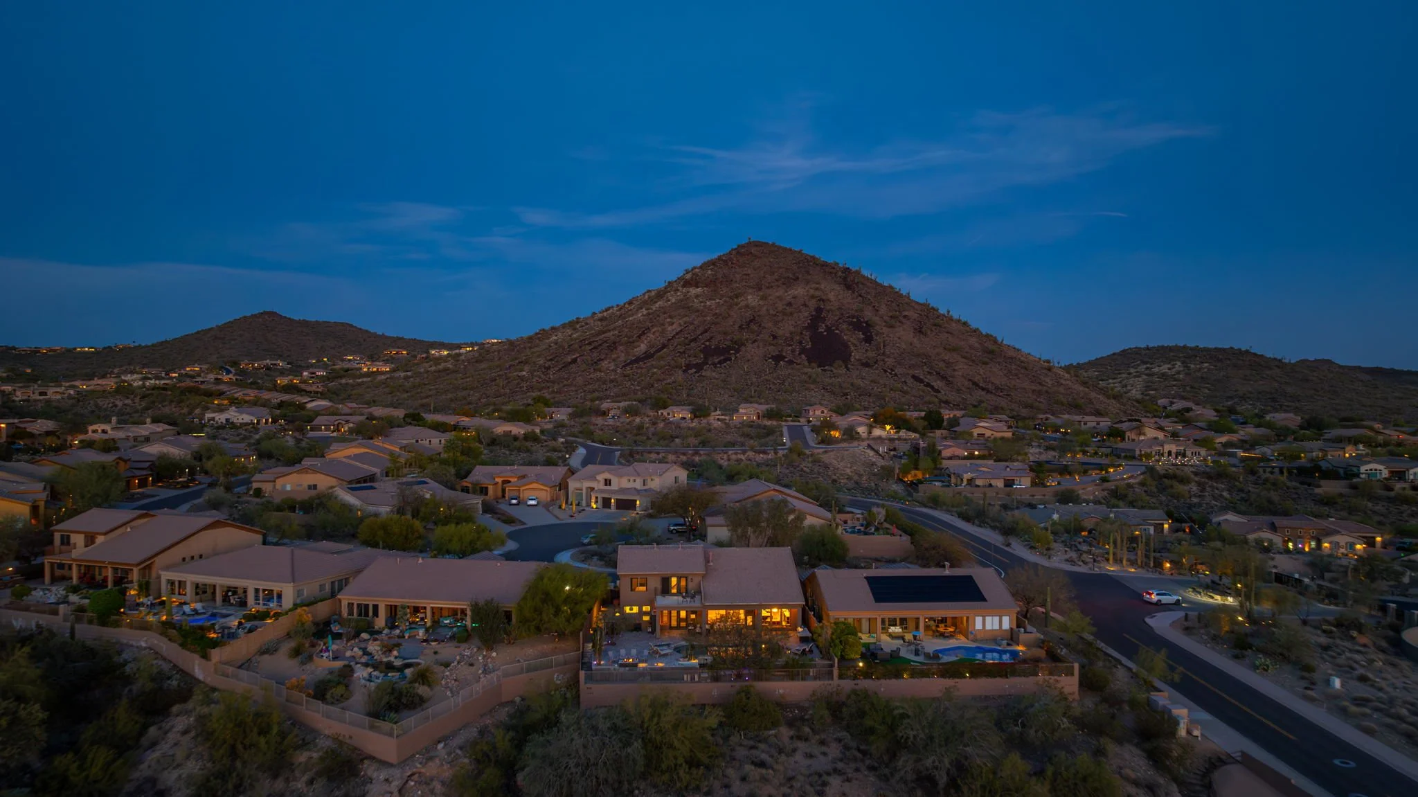 Aerial view of a suburban neighborhood at dusk with houses, winding roads, and a mountain in the background.