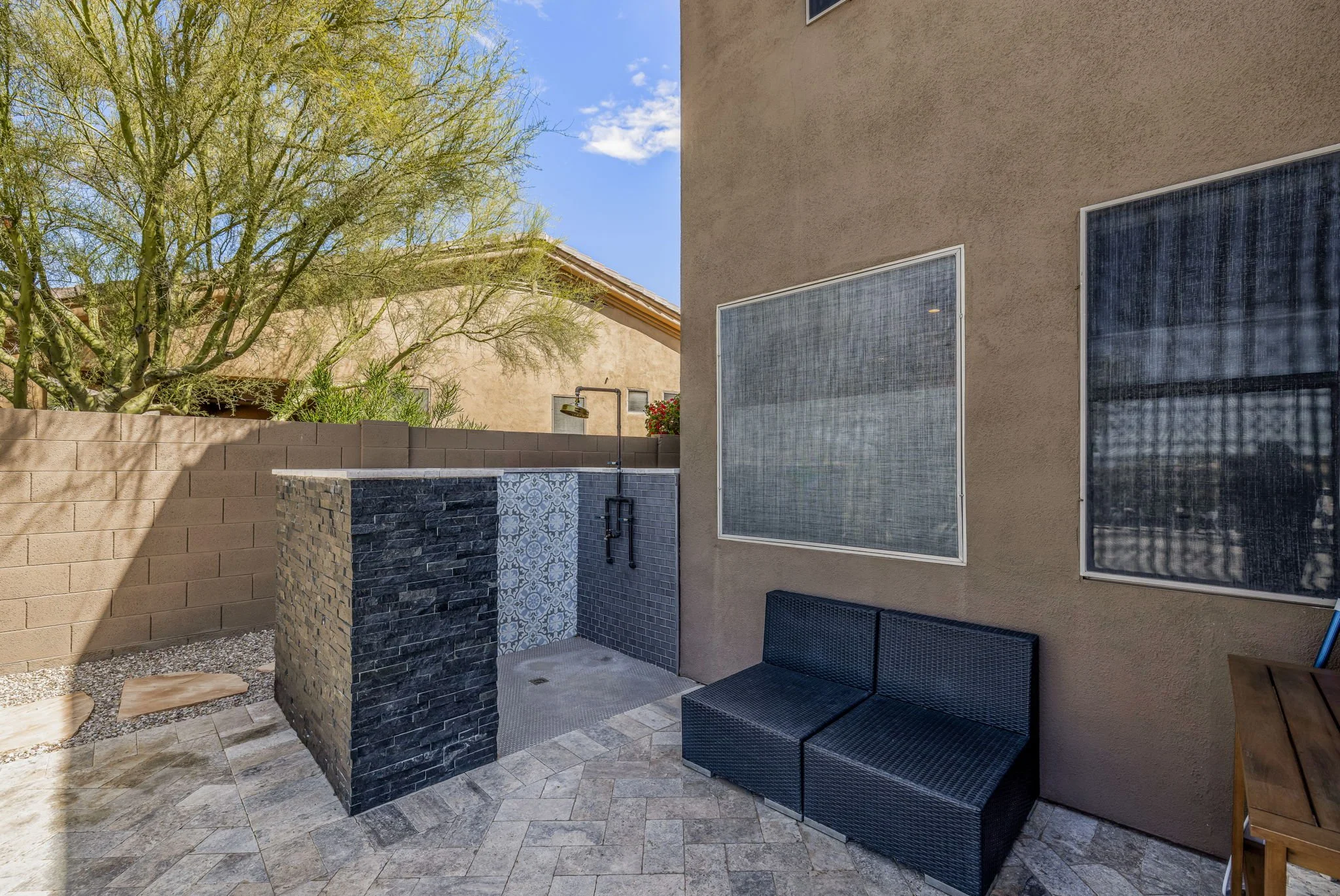 Outdoor patio with built-in shower, black wicker sofa, and large windows on beige stucco wall