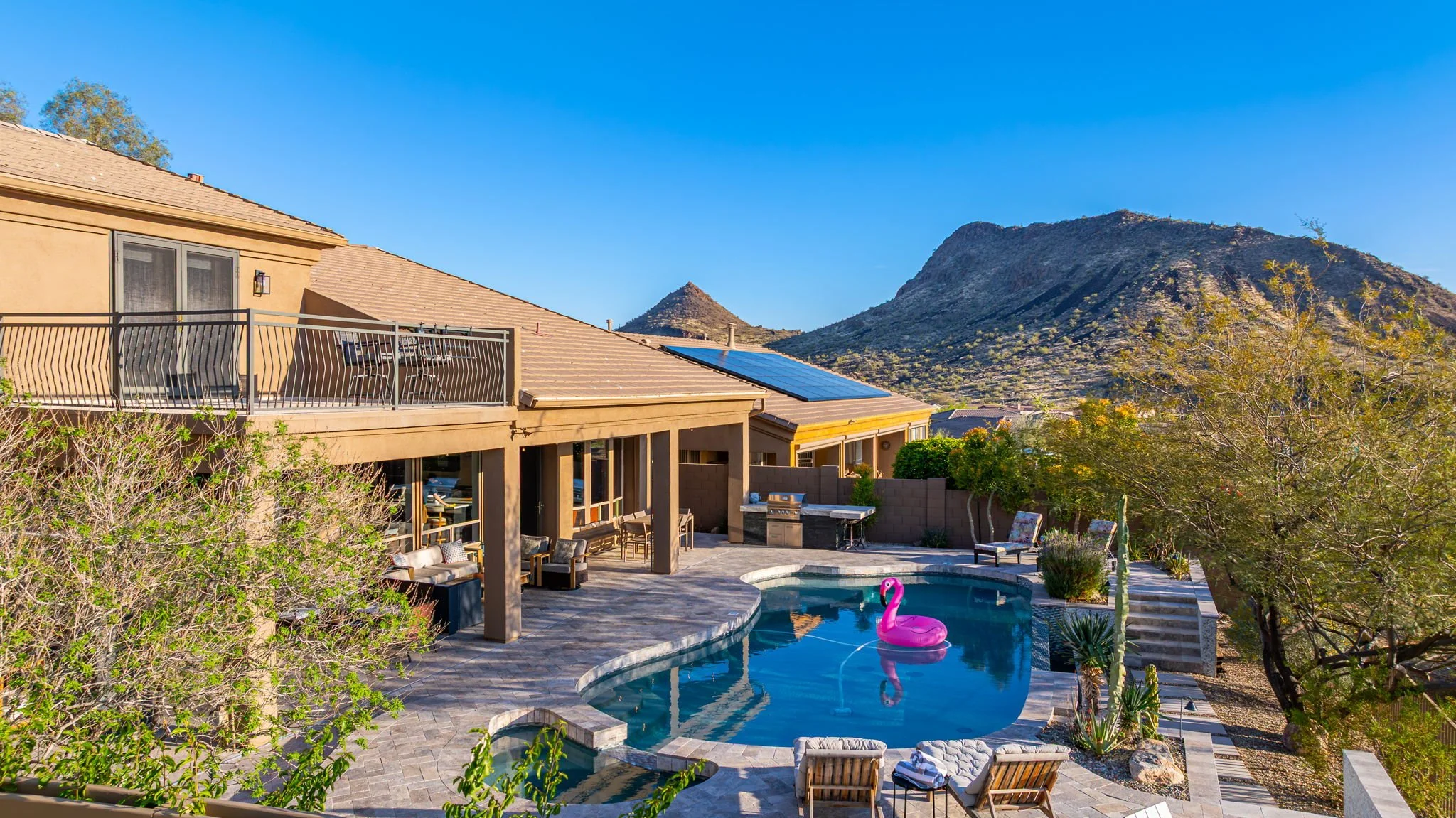 Backyard of a house with a swimming pool and outdoor seating, with mountains in the background and solar panels on the roof.
