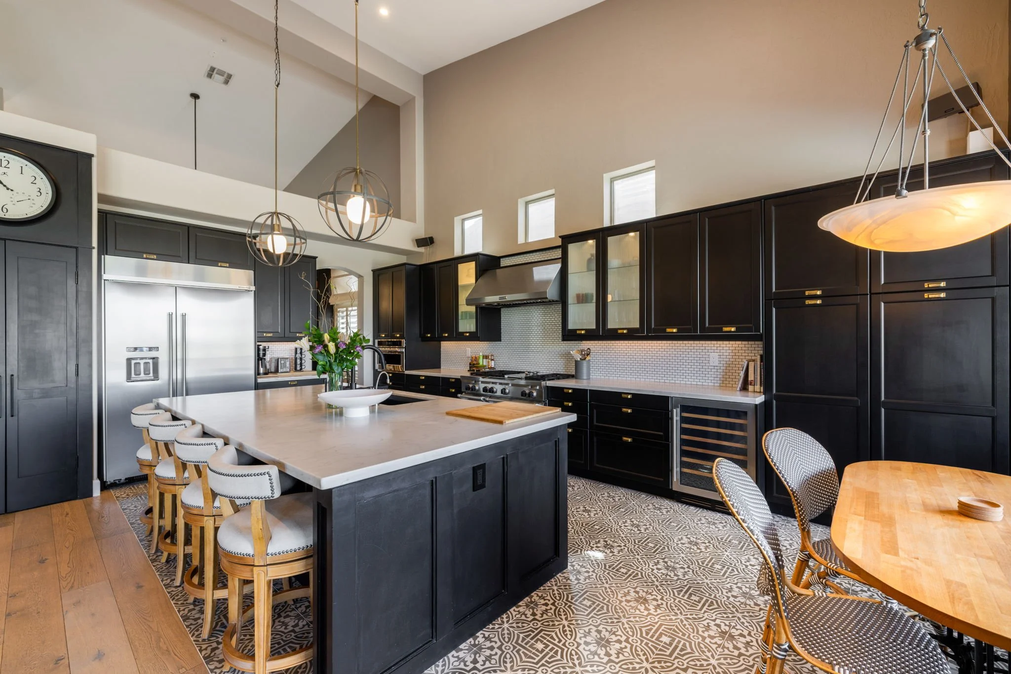 Modern kitchen with dark cabinets, white countertop island, stainless steel appliances, patterned floor tiles, and hanging pendant lights.