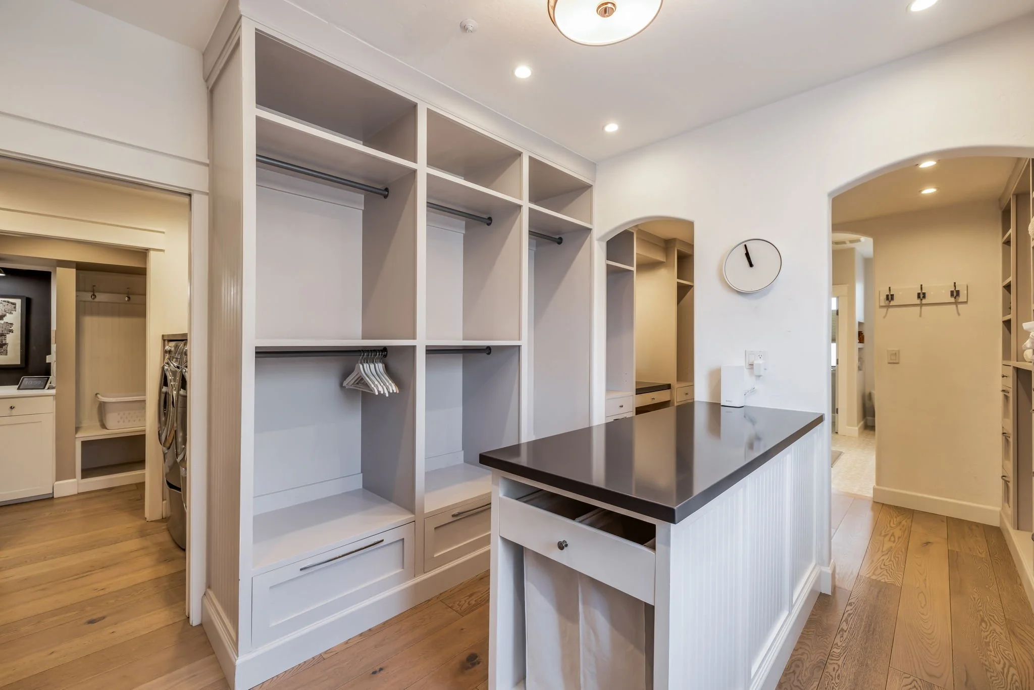 Empty walk-in closet with white shelves and drawers, black rod clothing hangers, dark countertop island, and wooden floors in a modern home interior.