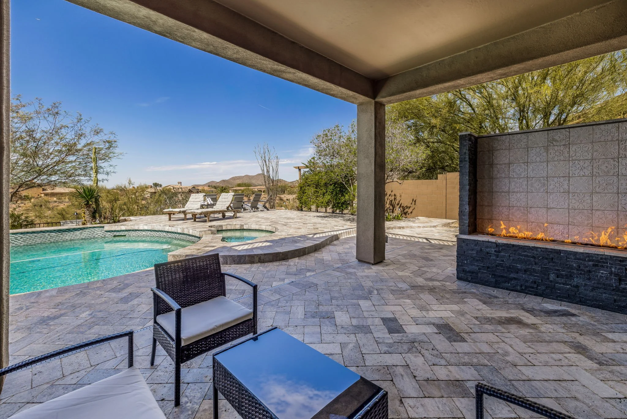 Outdoor pool patio with lounge chairs, trees, and a mountain view, featuring a modern fire feature on the right.