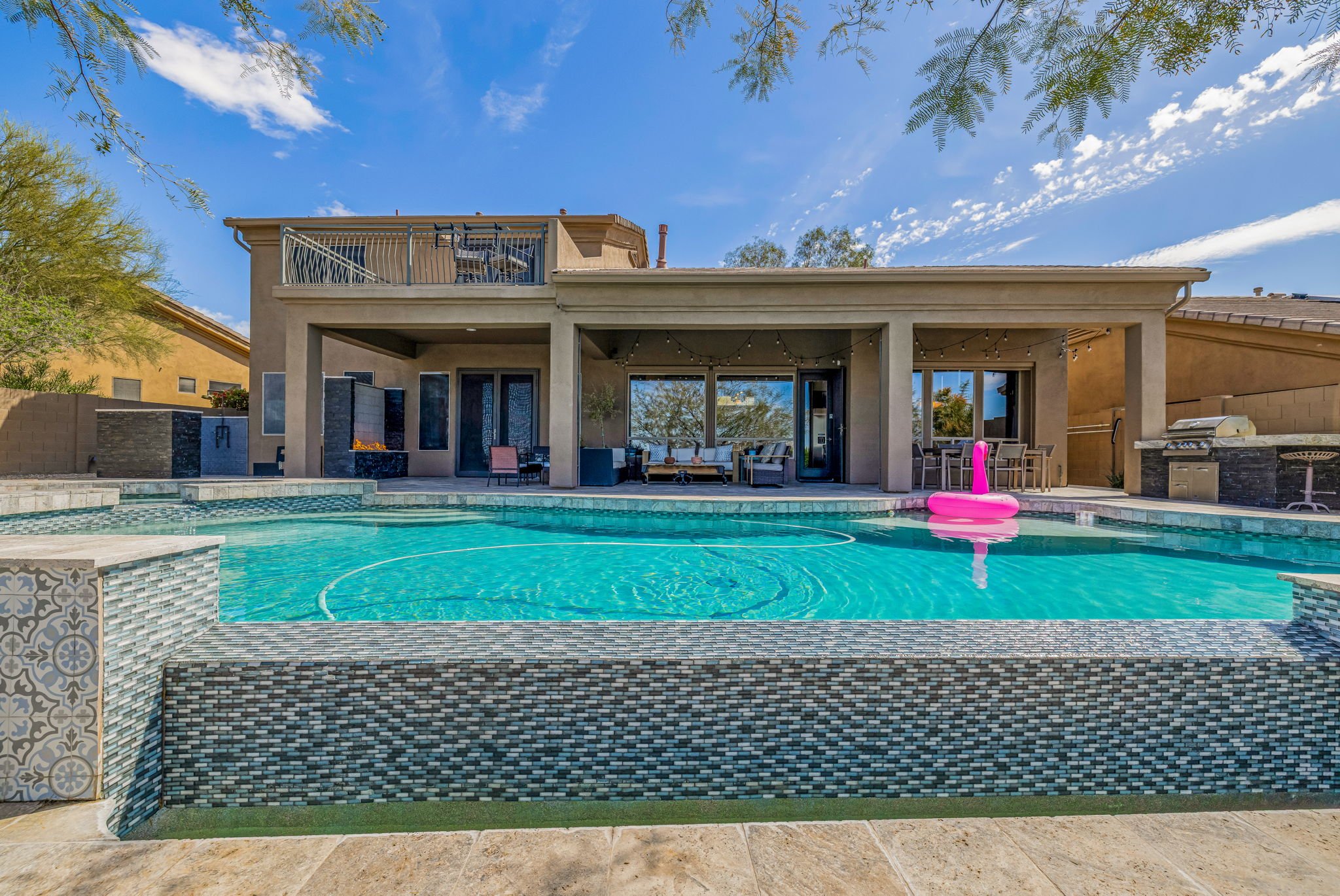Backyard with a pool, outdoor seating area, and a second-story balcony on a clear sunny day.