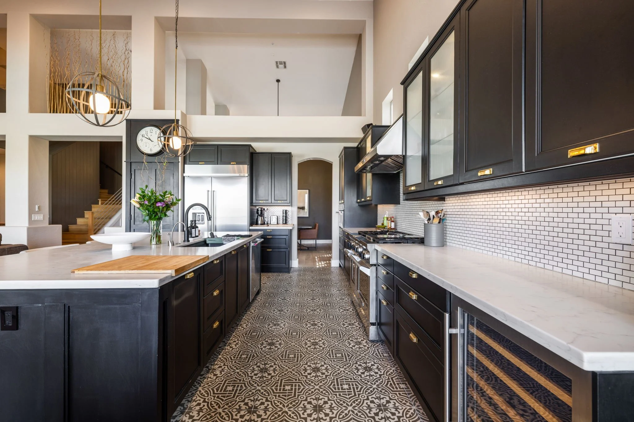 Modern kitchen with black cabinets, white countertops, patterned tile floor, and pendant lighting.