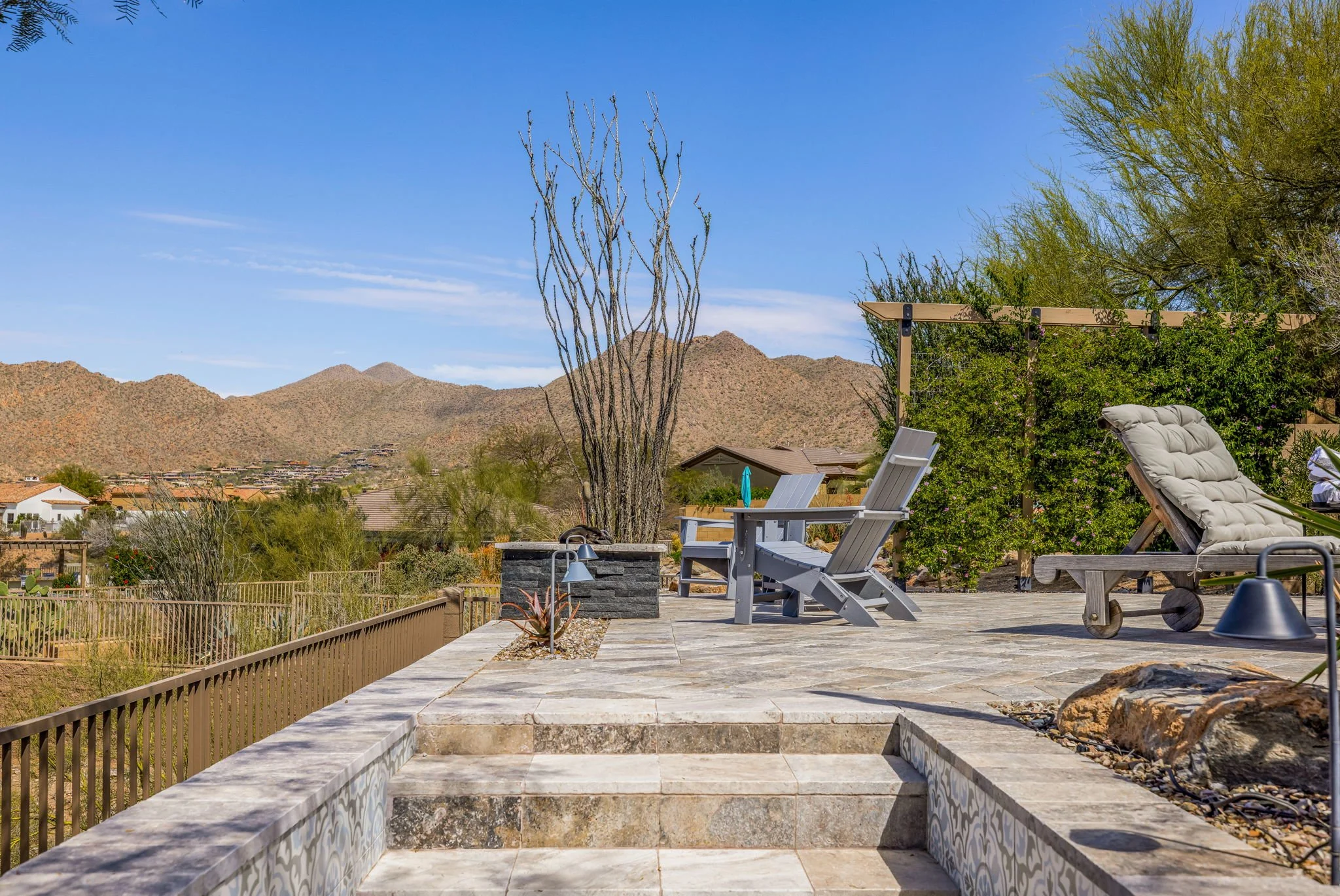 Outdoor patio with lounge chairs, potted plants, and desert landscape with mountains in the background under a clear blue sky.