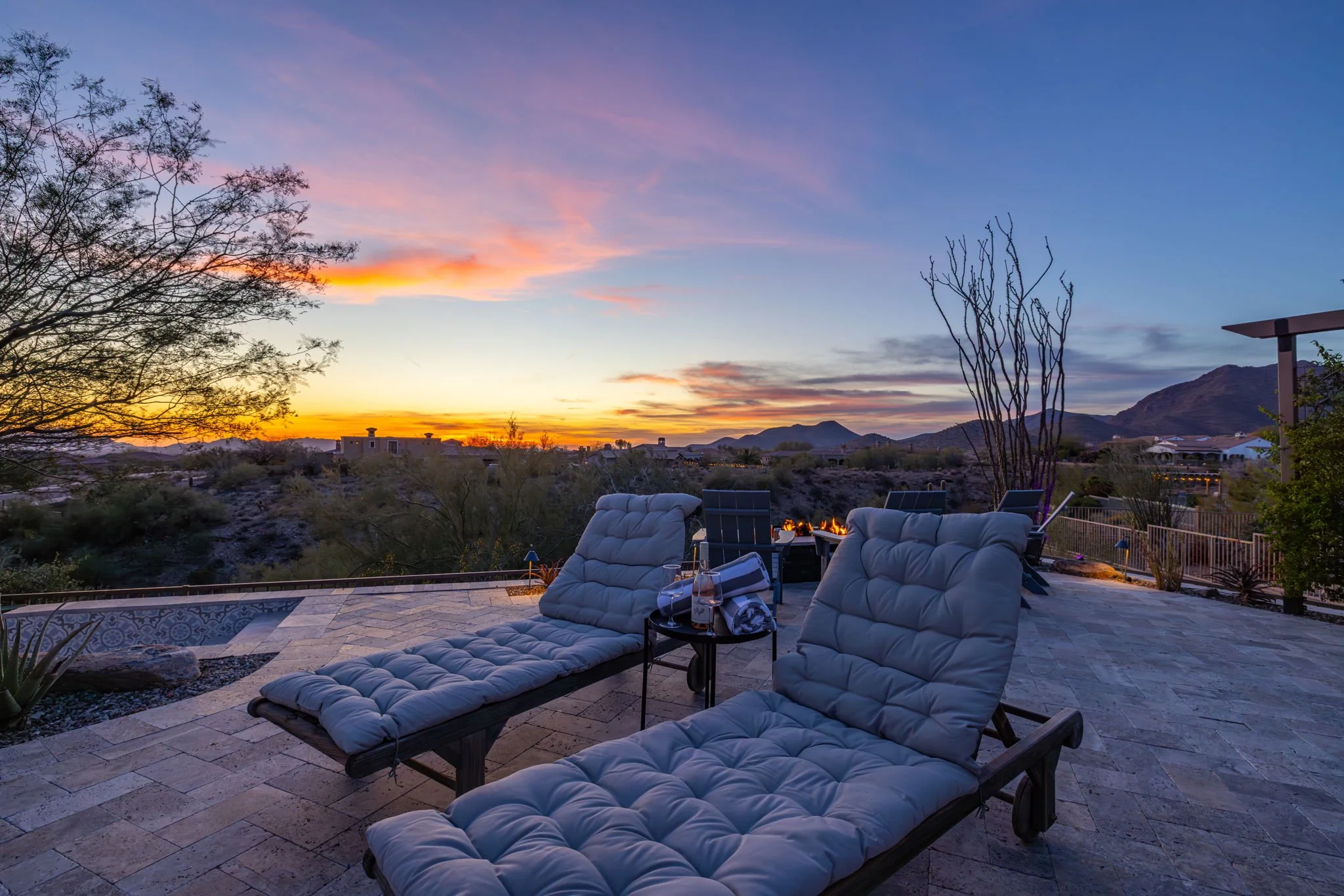 Outdoor patio with loungers, fire pit, and mountain view during sunset.