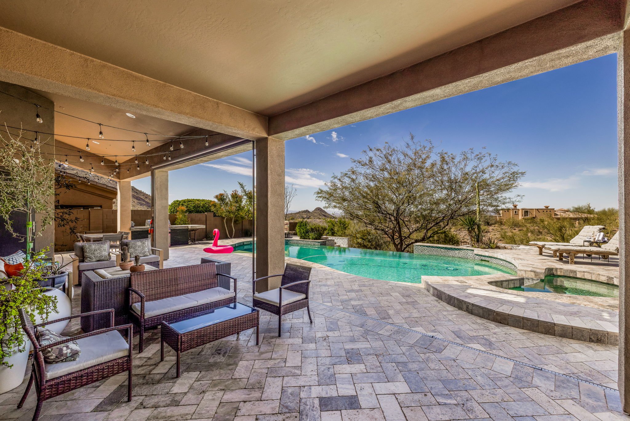 Outdoor patio with seating area, swimming pool, and desert landscape view under clear blue sky.