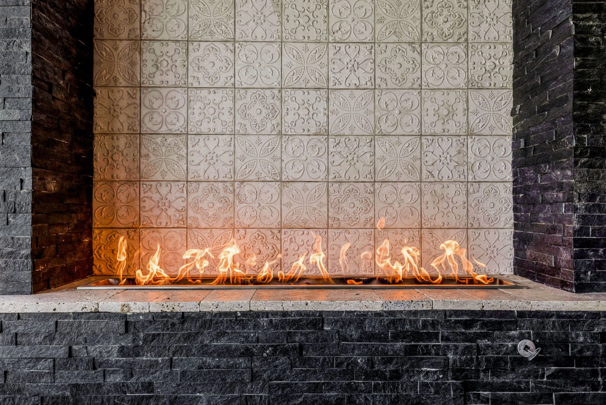 Modern fireplace with decorative tiles behind flames, black stone sides, and a control knob at the bottom right.