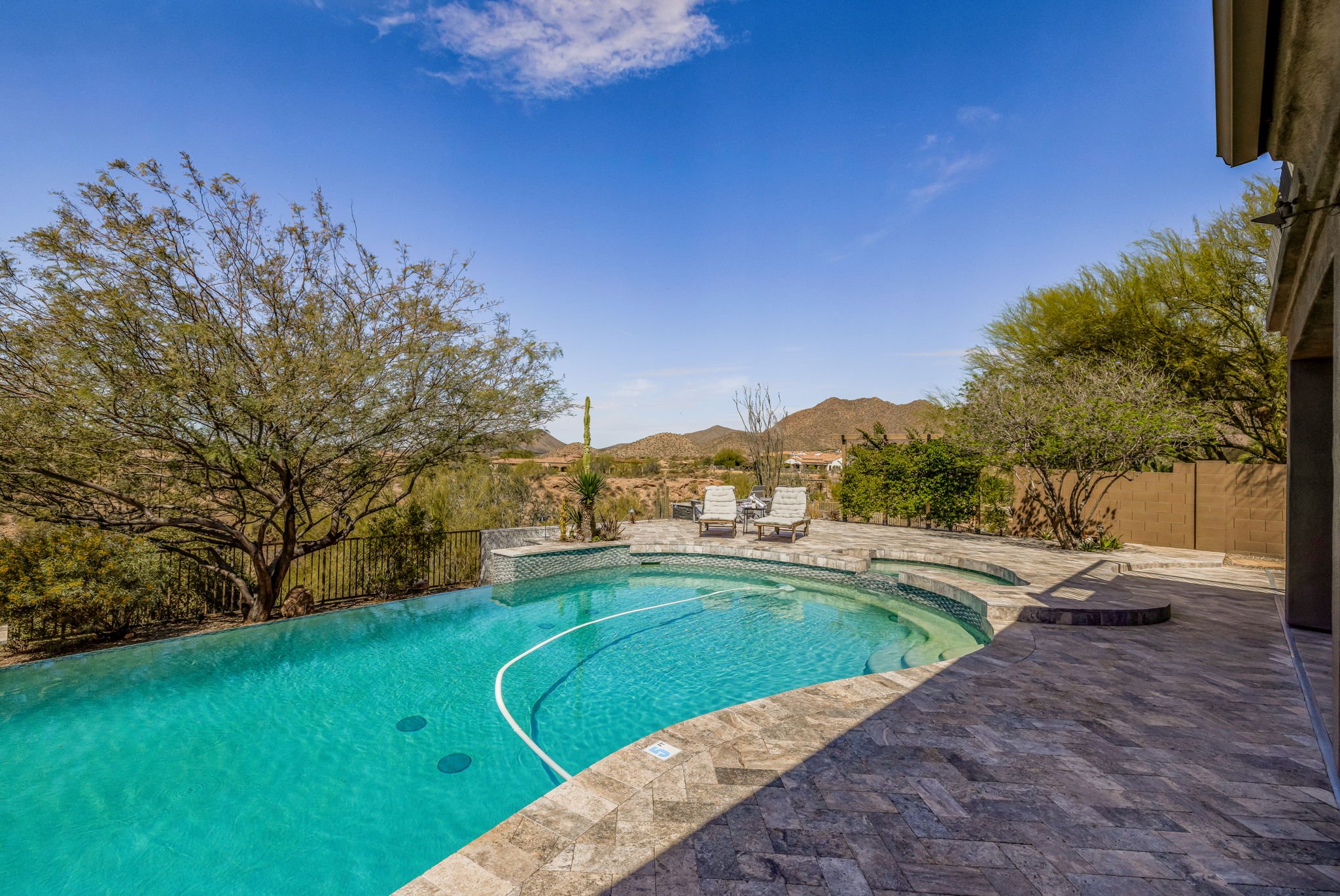 Poolside patio with two lounge chairs, surrounded by desert landscape and mountains under a blue sky.