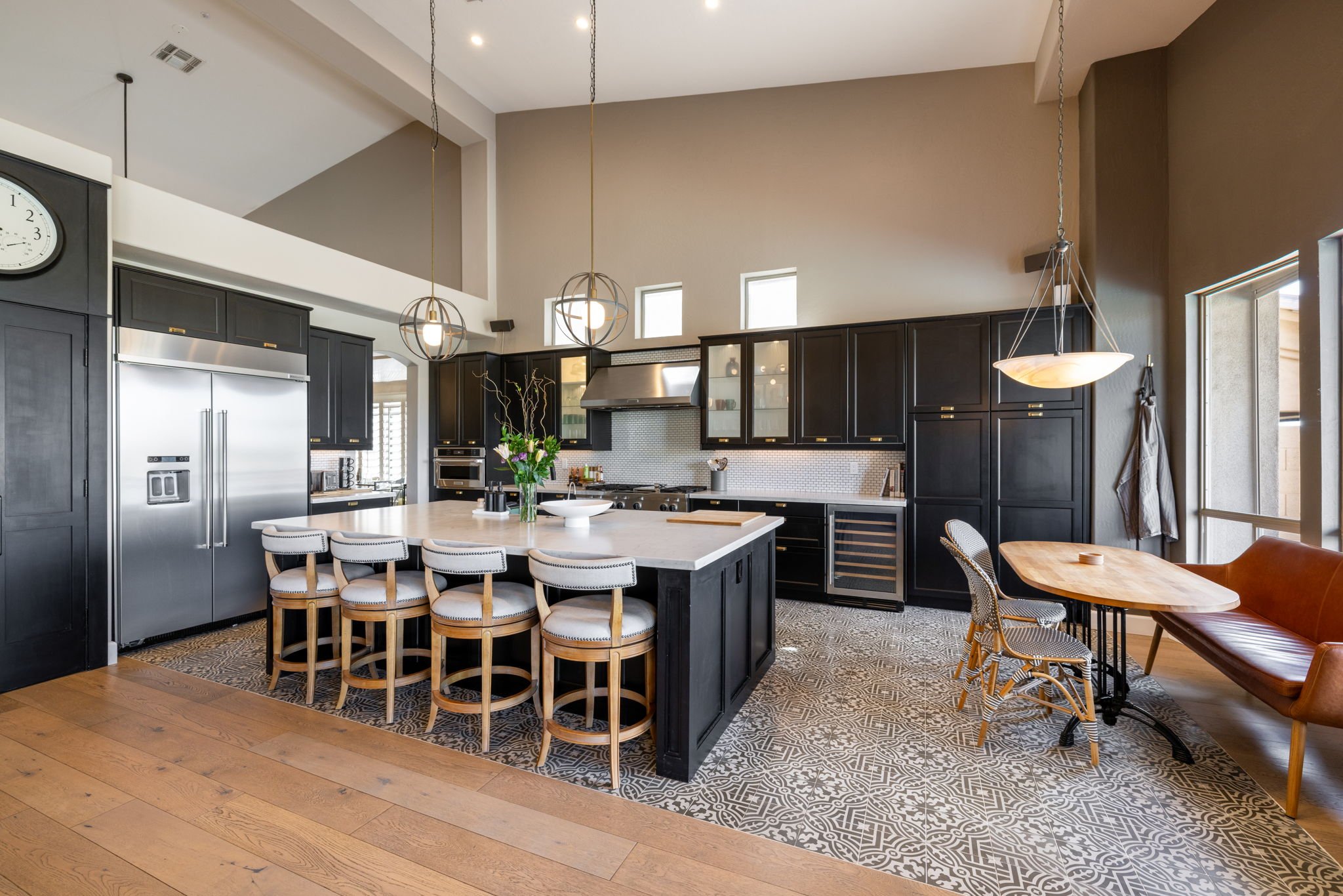 Modern kitchen with black cabinets, stainless steel appliances, a large island with seating, and a small dining area with a wooden table and chairs.