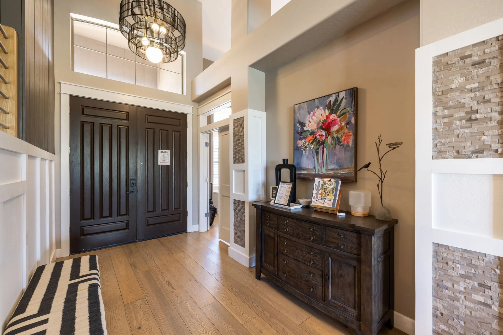 Entryway with dark wood front door, a bench with black and white stripes, a sideboard with decorative items, a large floral painting, and textured wall accents.
