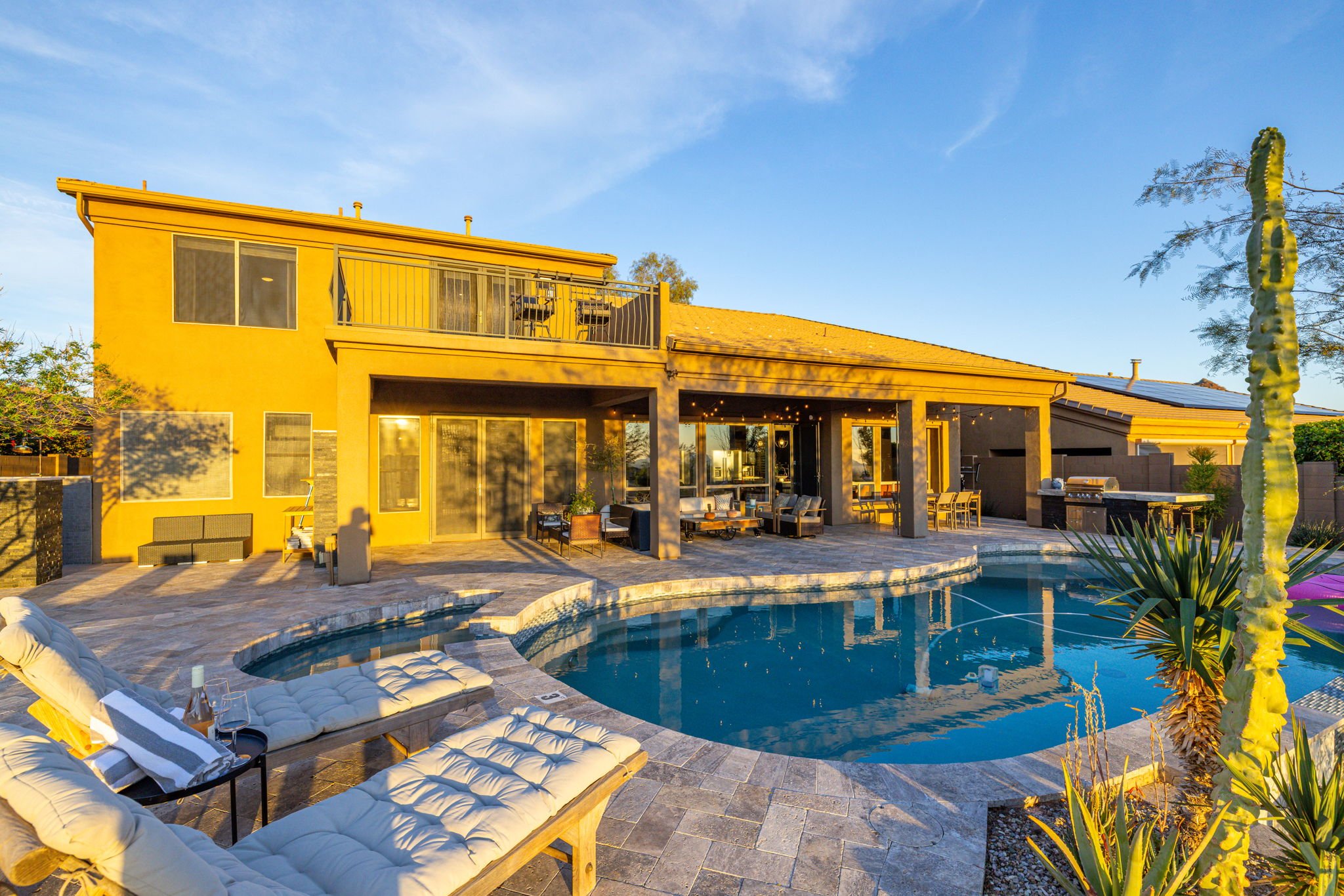 Backyard view of a two-story house with a swimming pool, outdoor seating area, and patio in the evening light.