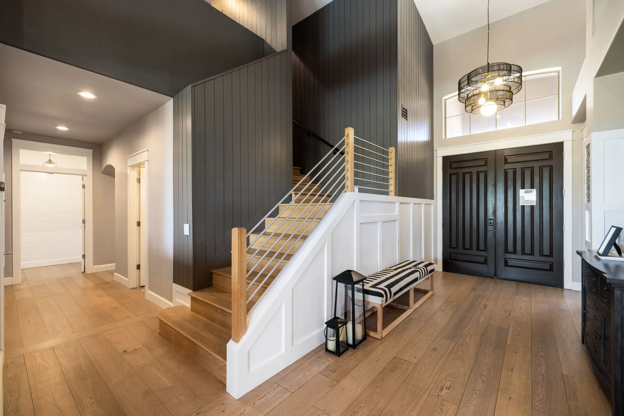 Entryway with wooden flooring, black front doors, a black and white bench, and candle lanterns, with a staircase leading upstairs.