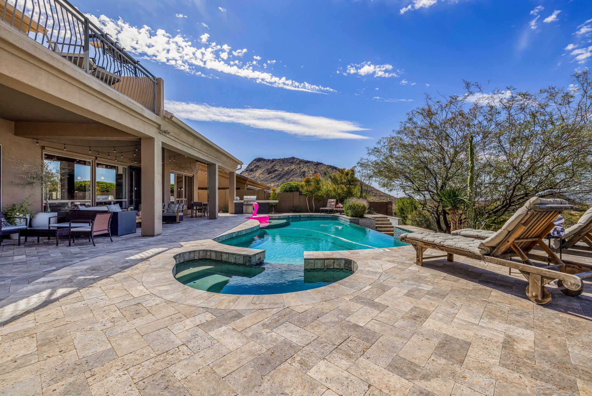 Backyard with swimming pool, lounge chairs, trees, and mountain in the background under a blue sky with clouds.