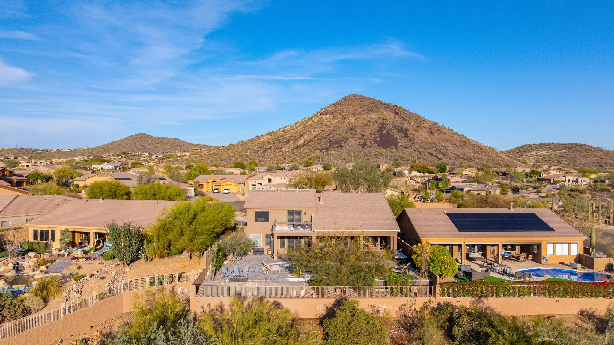 Aerial view of a suburban neighborhood with single-family houses, desert landscaping, and mountains in the background under a blue sky.