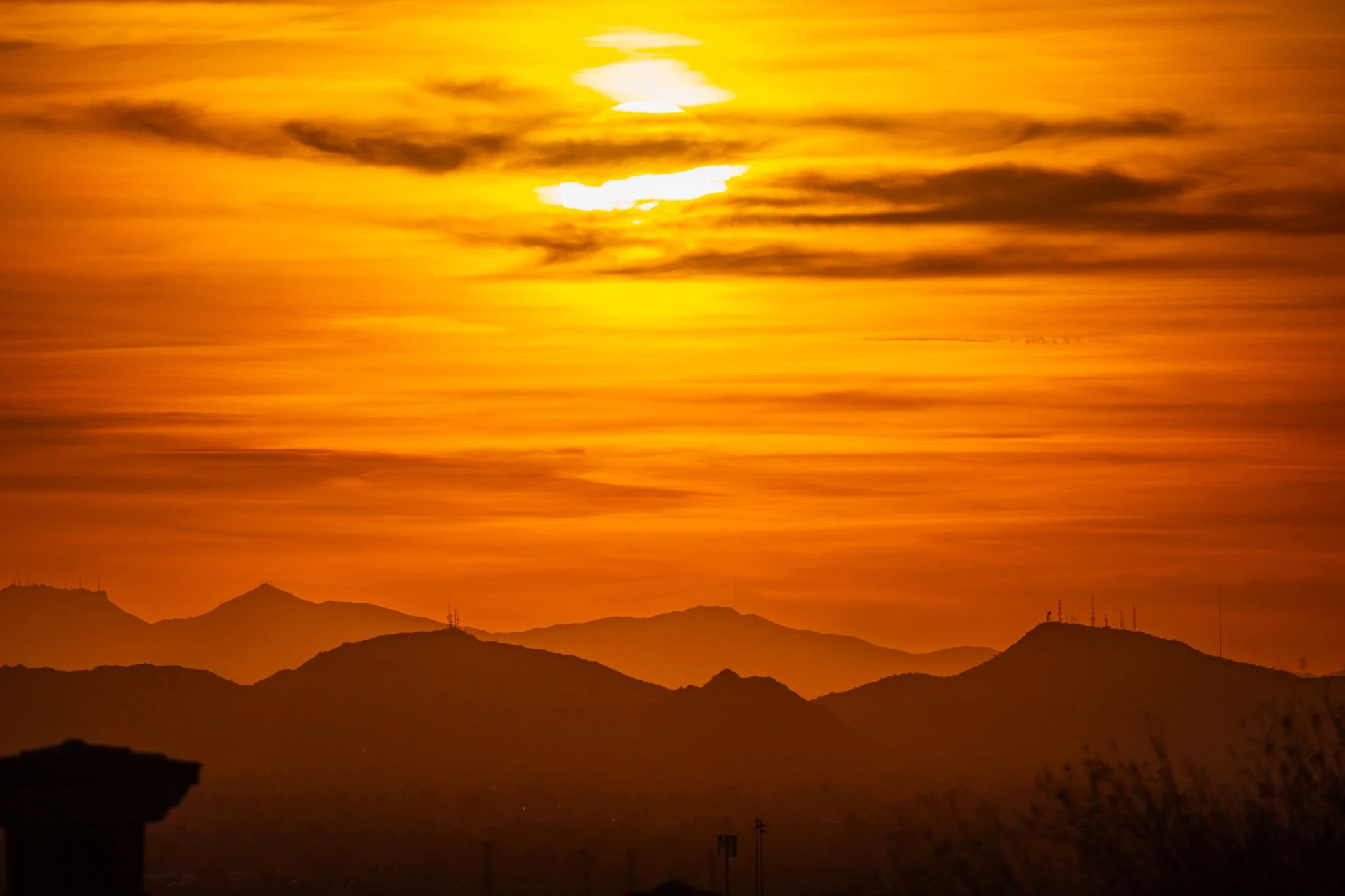 Sun setting over orange-hued mountains and cloudy sky.