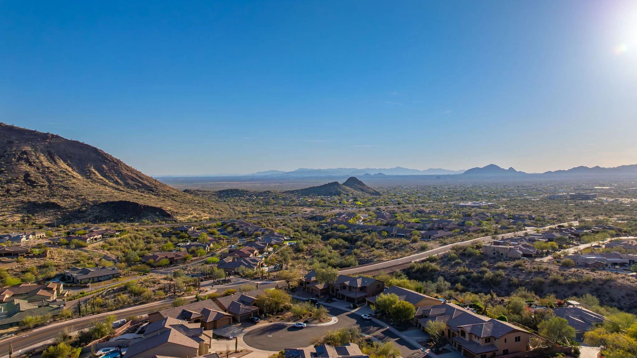 Aerial view of a suburban neighborhood in a desert landscape with mountains in the distance, under a clear blue sky.