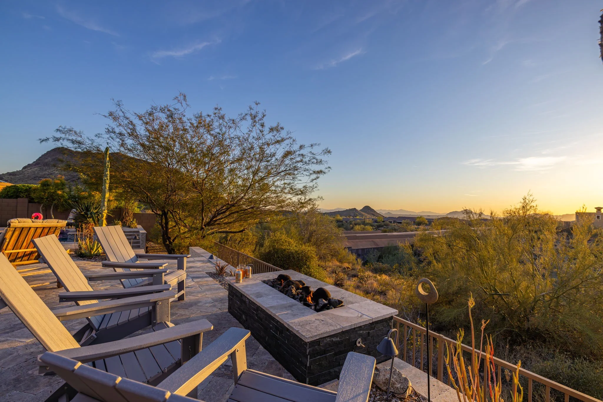 Outdoor patio with wooden chairs and a fire pit overlooking a desert landscape at sunset.