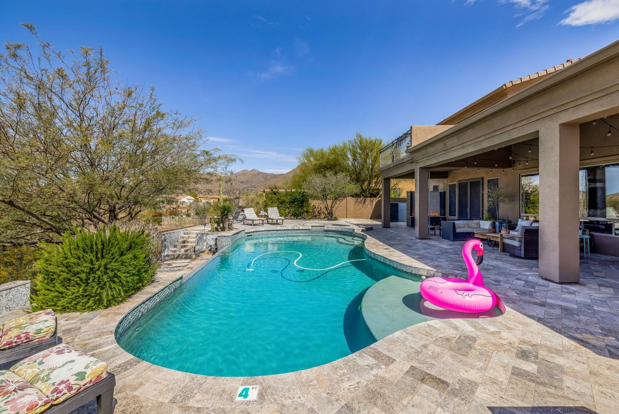 A backyard with a swimming pool, lounge chairs, and outdoor seating area, with desert mountains in the background.