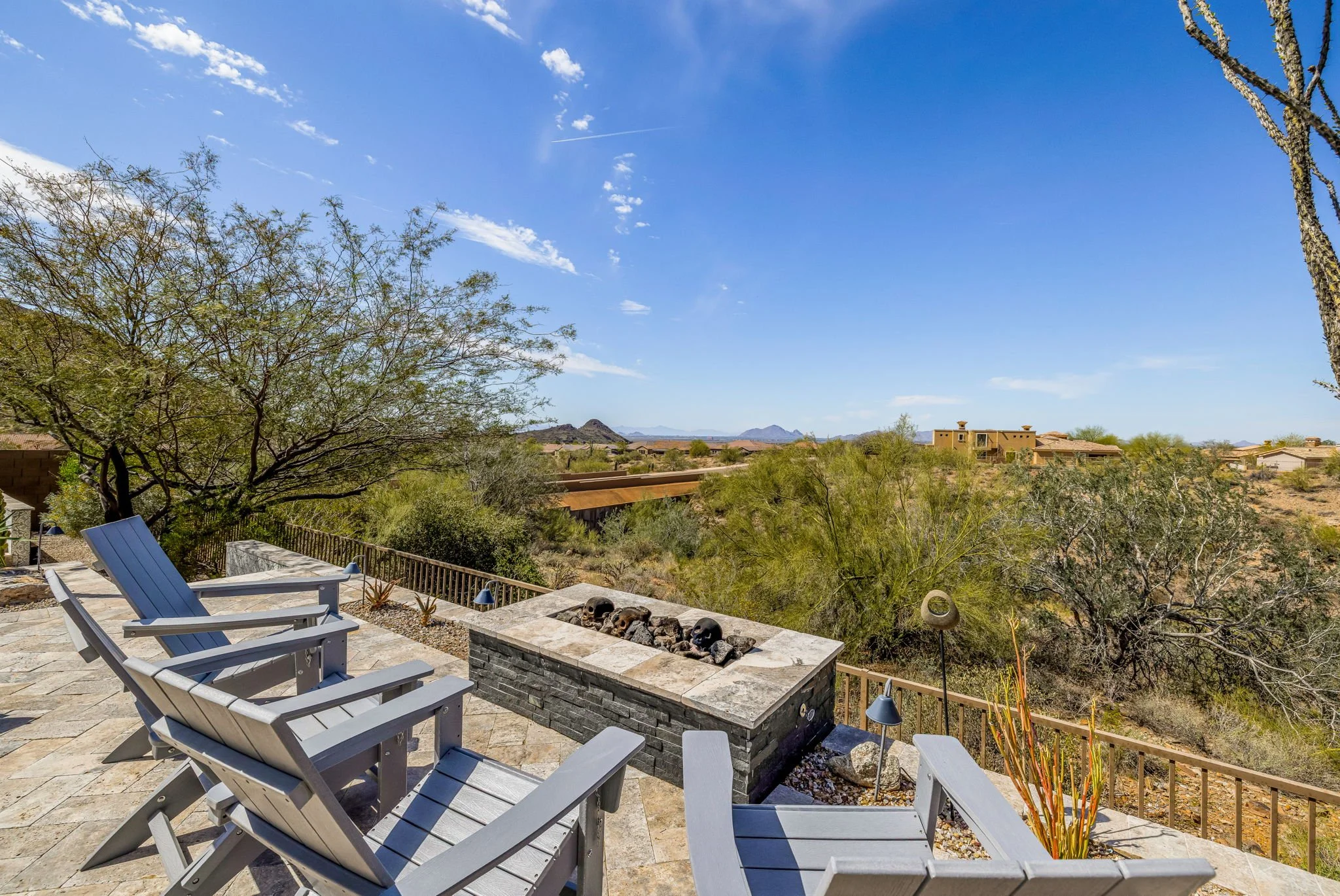 Patio with modern chairs and a firepit overlooking desert landscape and mountains under a clear blue sky.