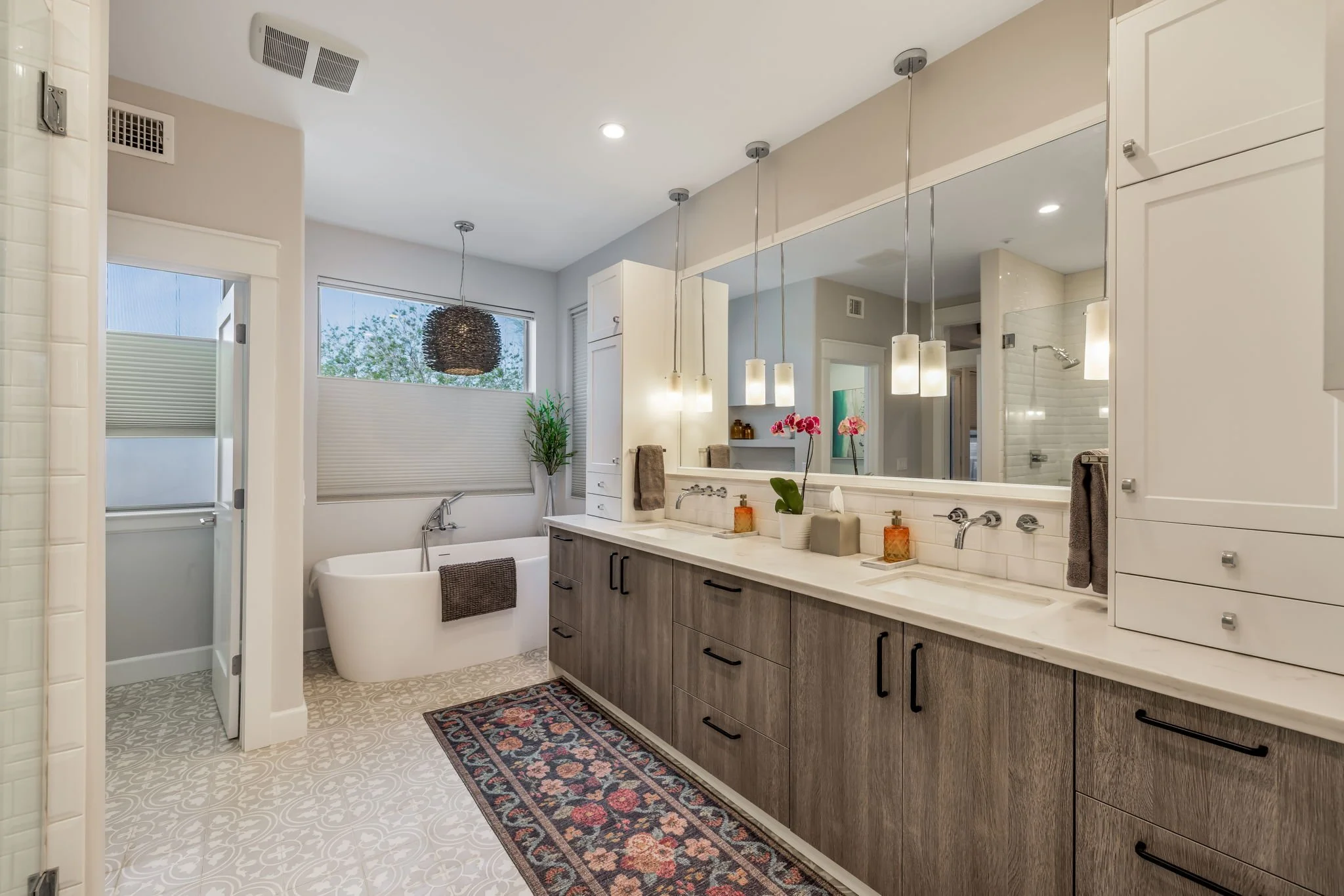 Modern bathroom with double sink vanity, large mirror, bathtub, and separate shower area, decorated with plants and flowers.