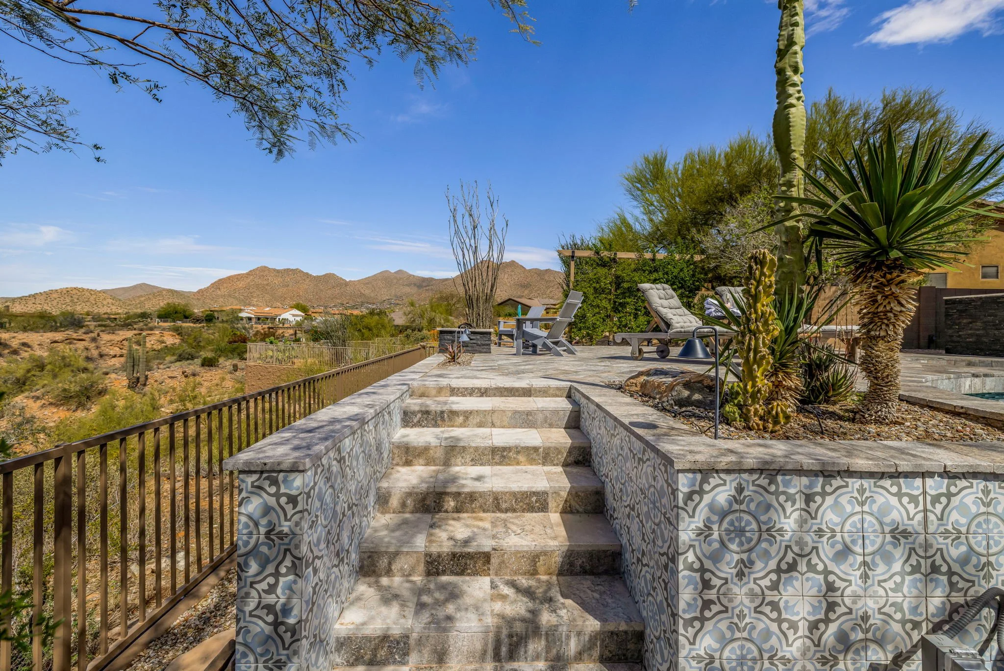 A desert backyard patio with patterned tile stairs, desert flora, and mountain views.
