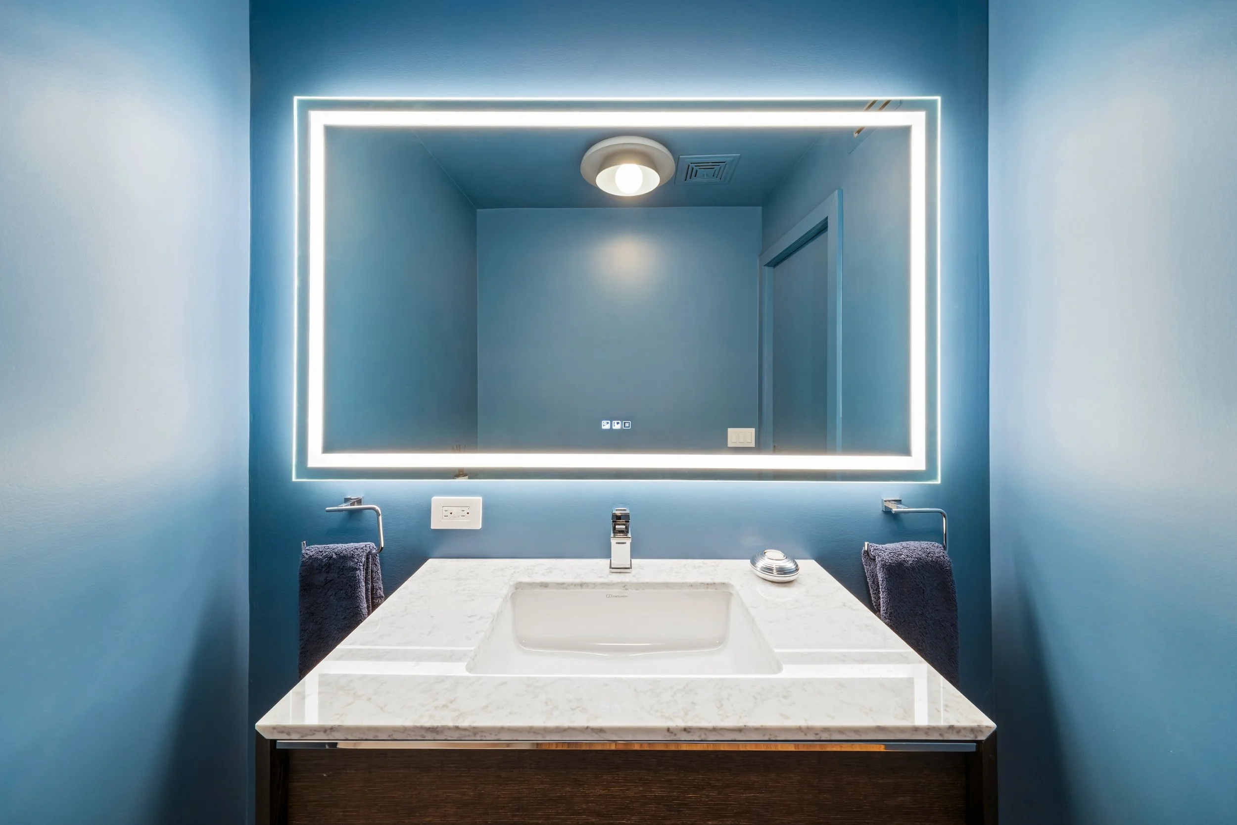 Luxury bathroom redesign featuring blue accent walls and illuminated LED mirror vanity in River North Chicago.