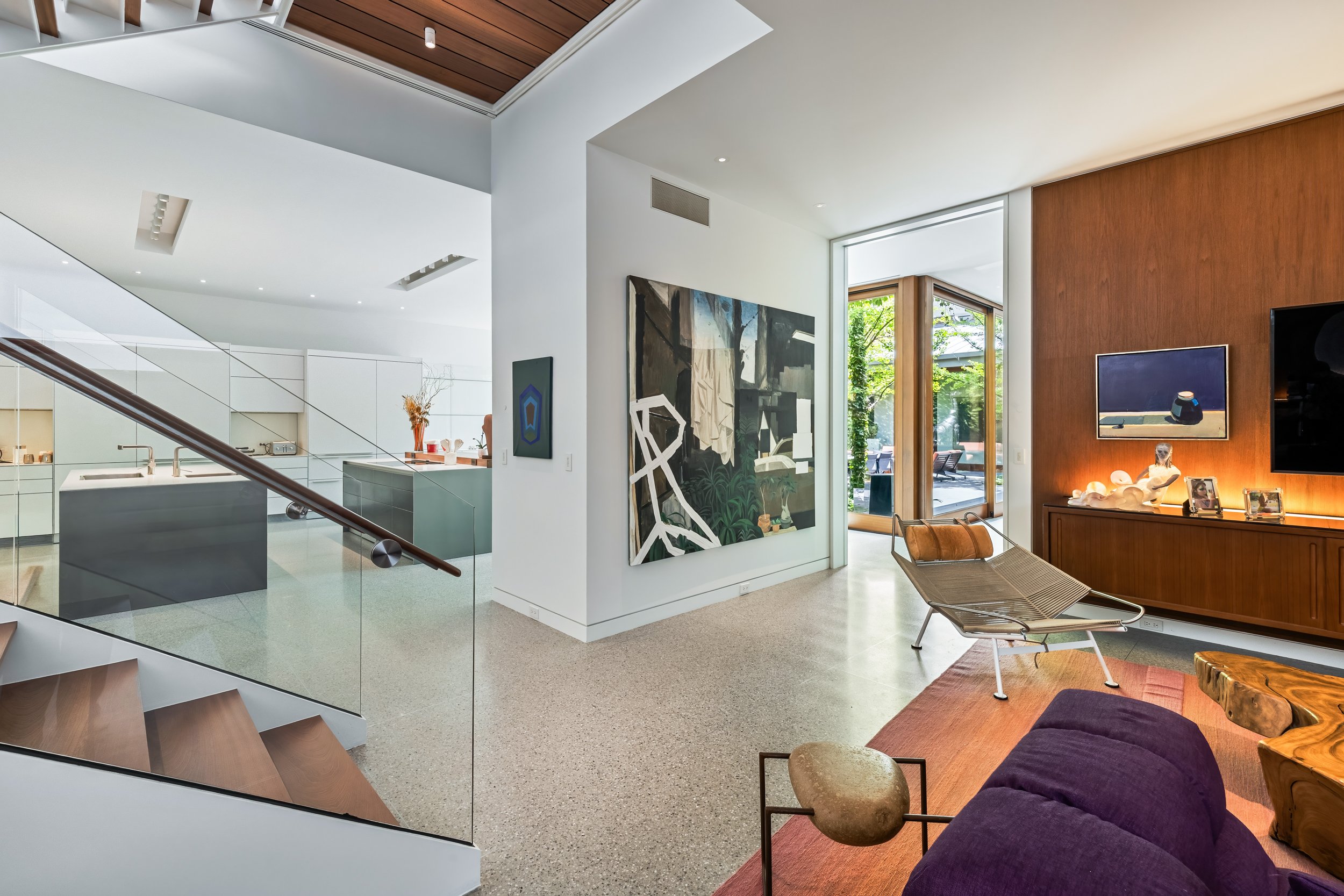 High-end architectural home re-design in Chicago with floating glass staircase, warm wood wall paneling, and open-plan living room.