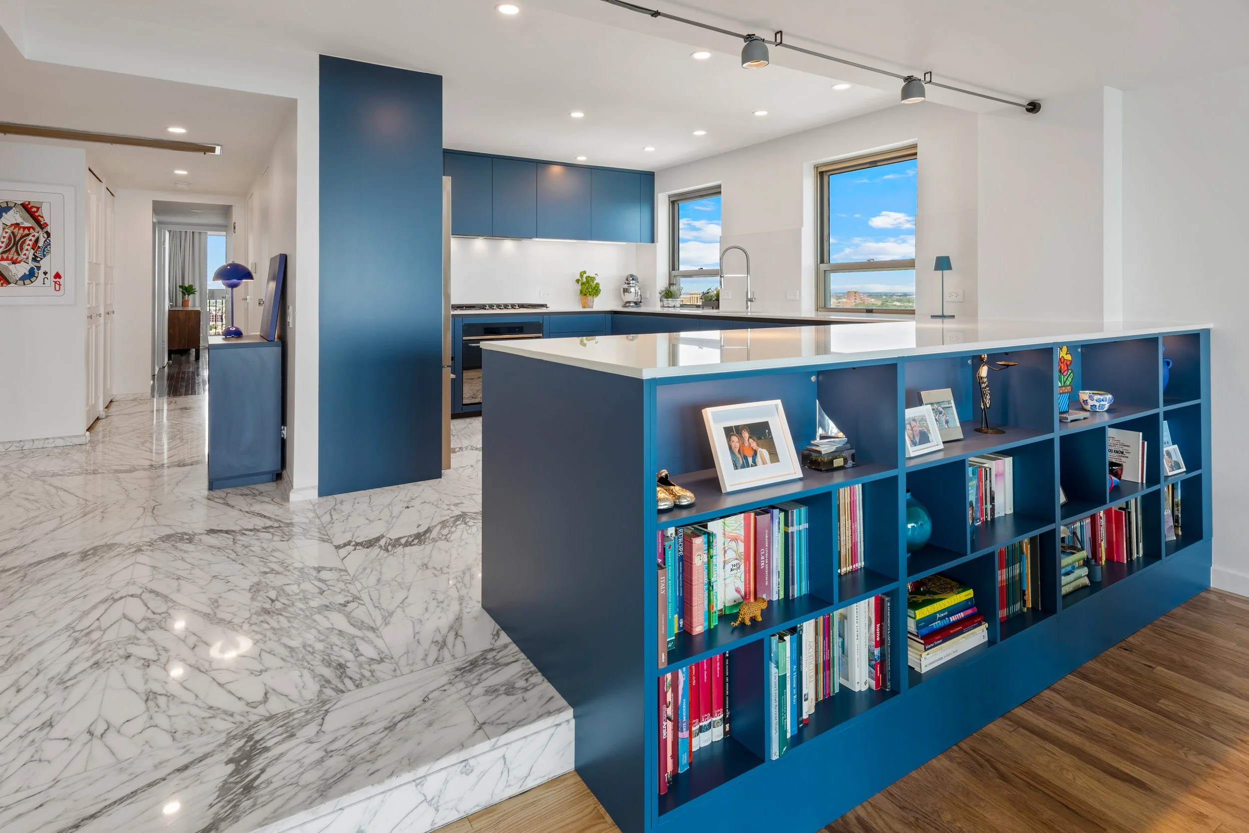 Open-concept Chicago condo gut rehab with custom cobalt blue low-profile bookcase room divider and white polished marble tile floors.