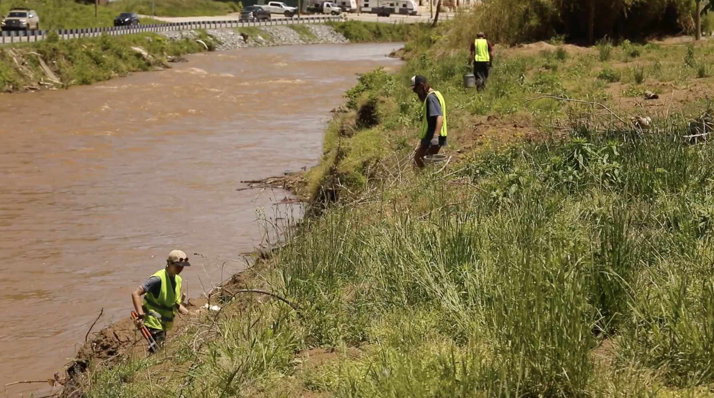 Along the riverbank, three cleanup crew members comb through flood debris to restore the French broad river.
