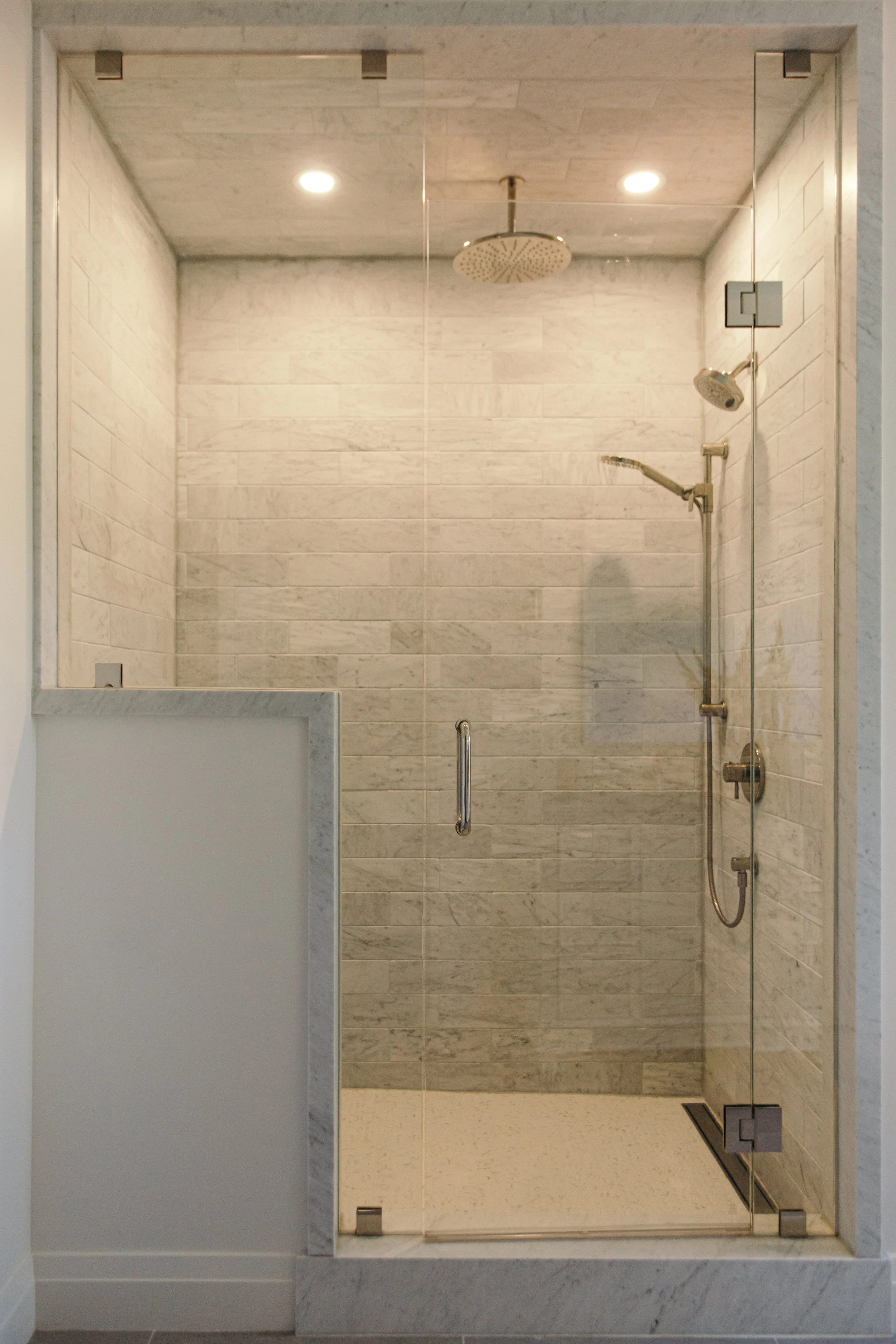 A wooden dresser with metal handles, topped with a glass vase of white flowers, framed photographs, a stack of books, and a table lamp, in a room with white walls and wood flooring.