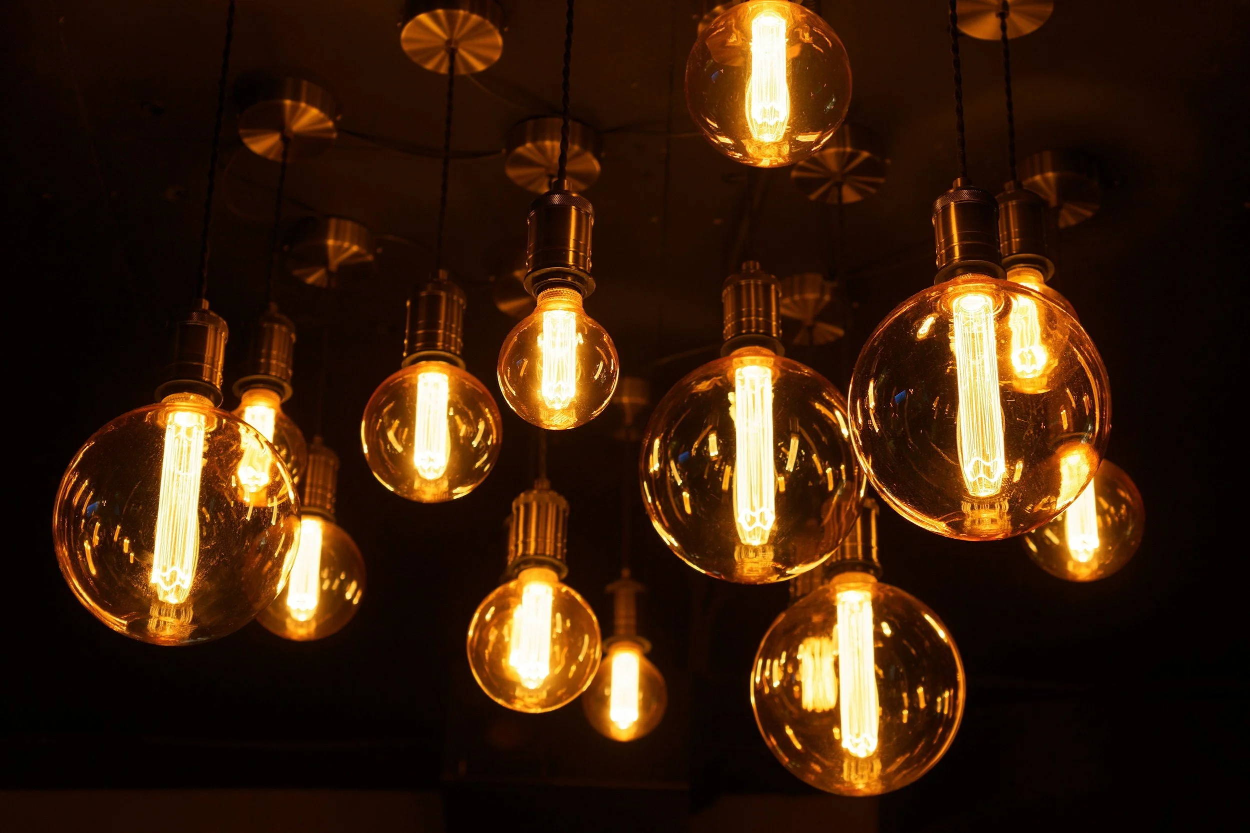 Multiple vintage-style Edison light bulbs with glowing filaments hanging from the ceiling in warm yellow-orange light.