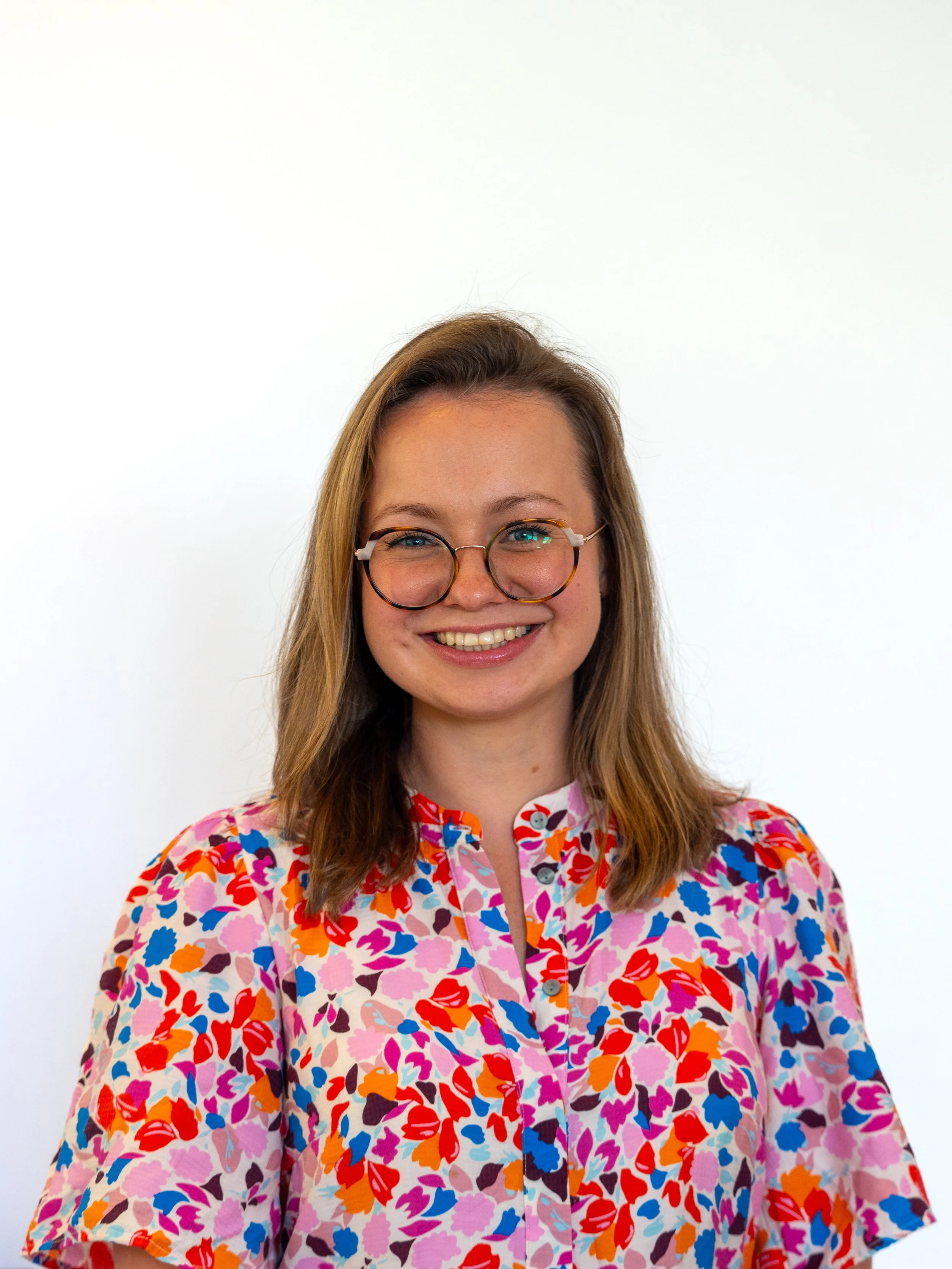Smiling woman with glasses in a colorful floral shirt against a plain white background.