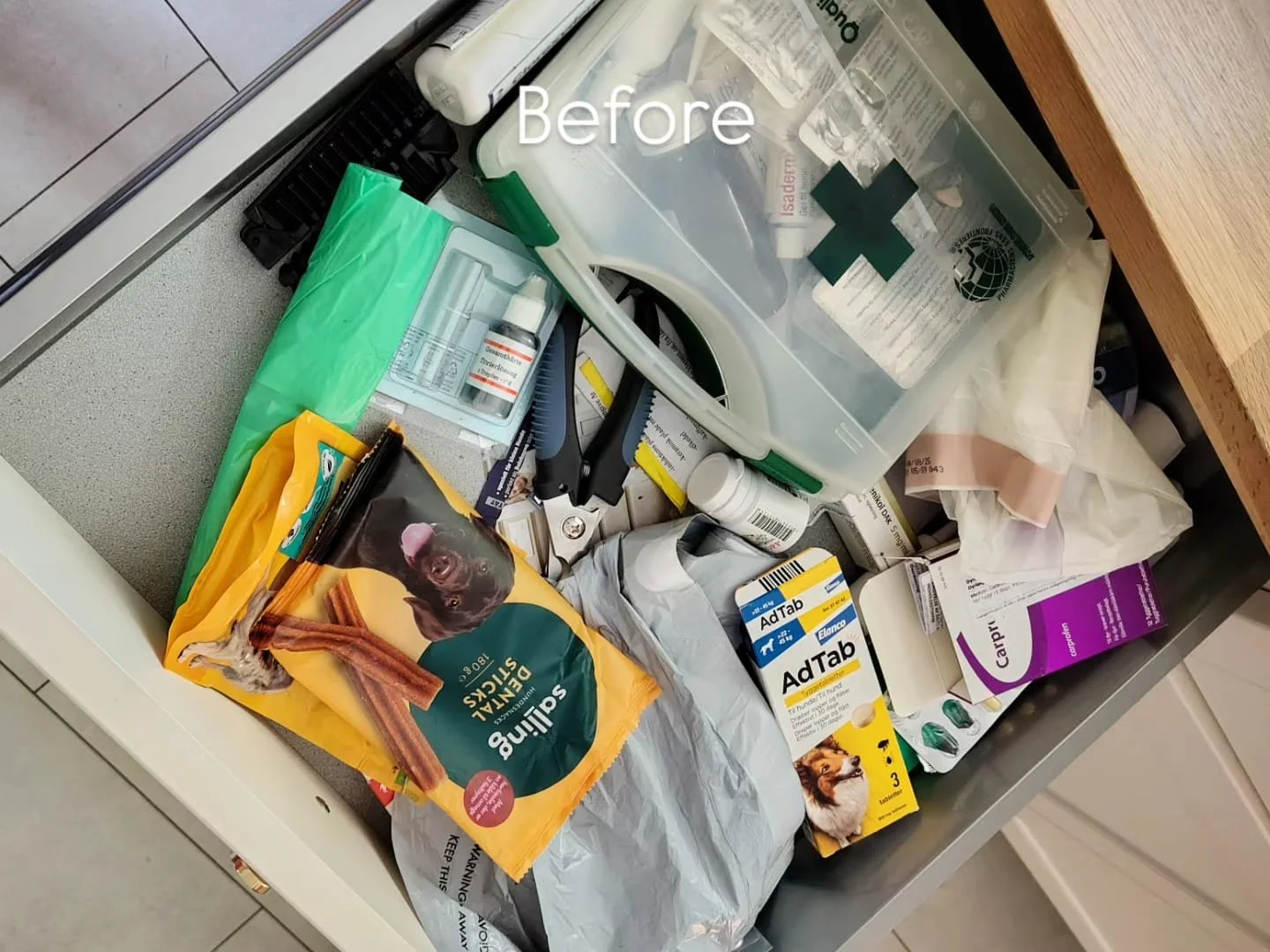 Disorganized kitchen drawer with various medicine bottles, packaging, and medical supplies, including an AdTab box, a first aid kit, and a bag of dental treats.