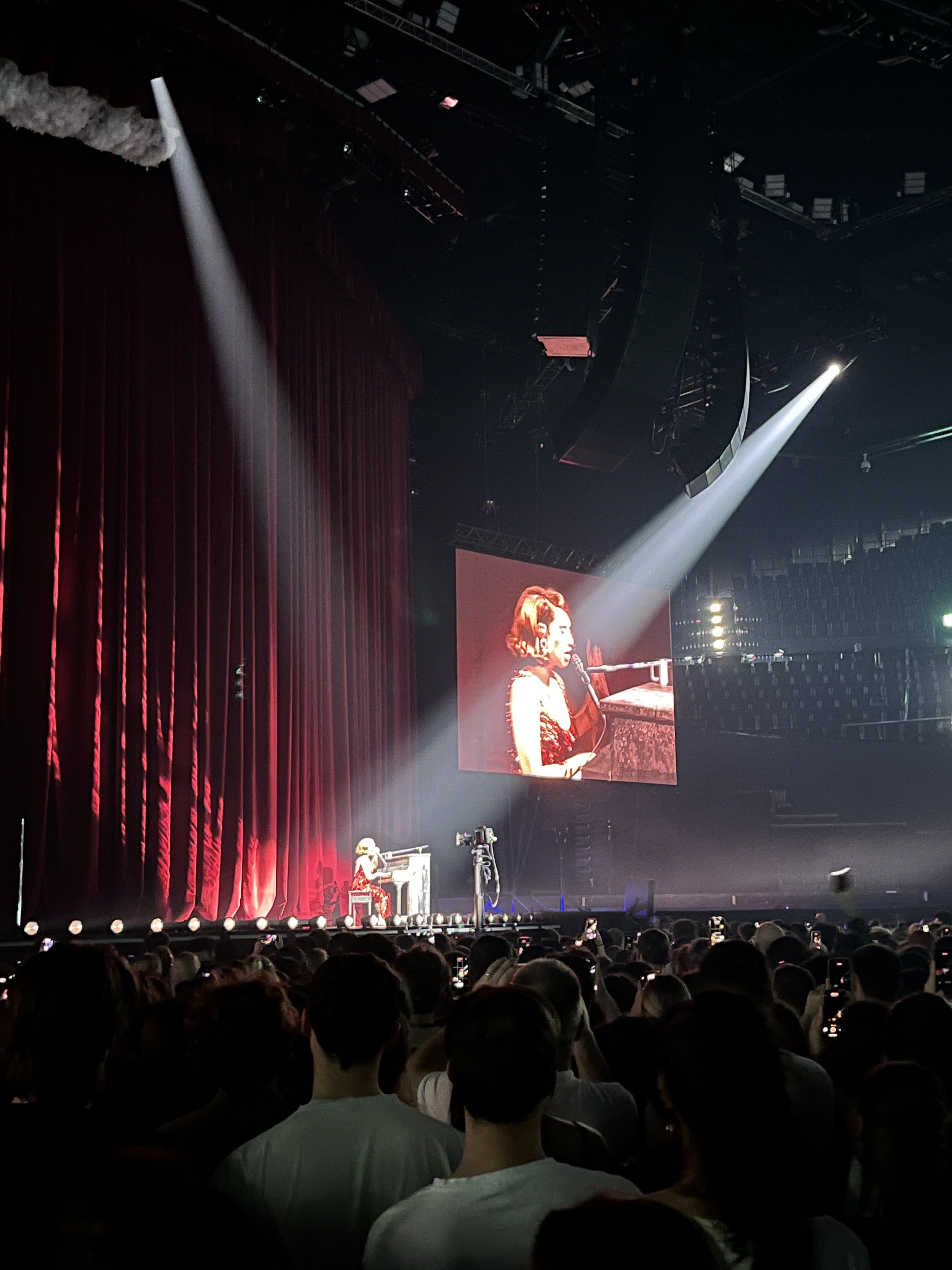 Raye in a sparkling red dress performing a song on the piano and singing