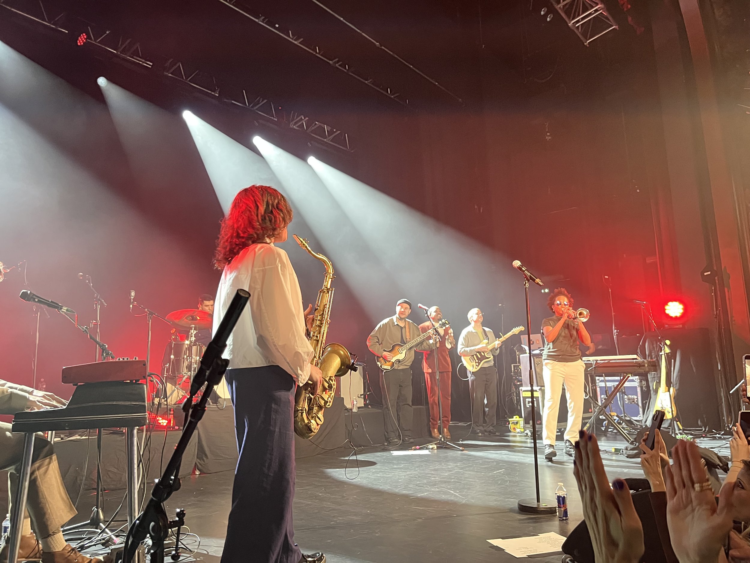 Saxophone and trumpet players on stage with other musicians in the background.