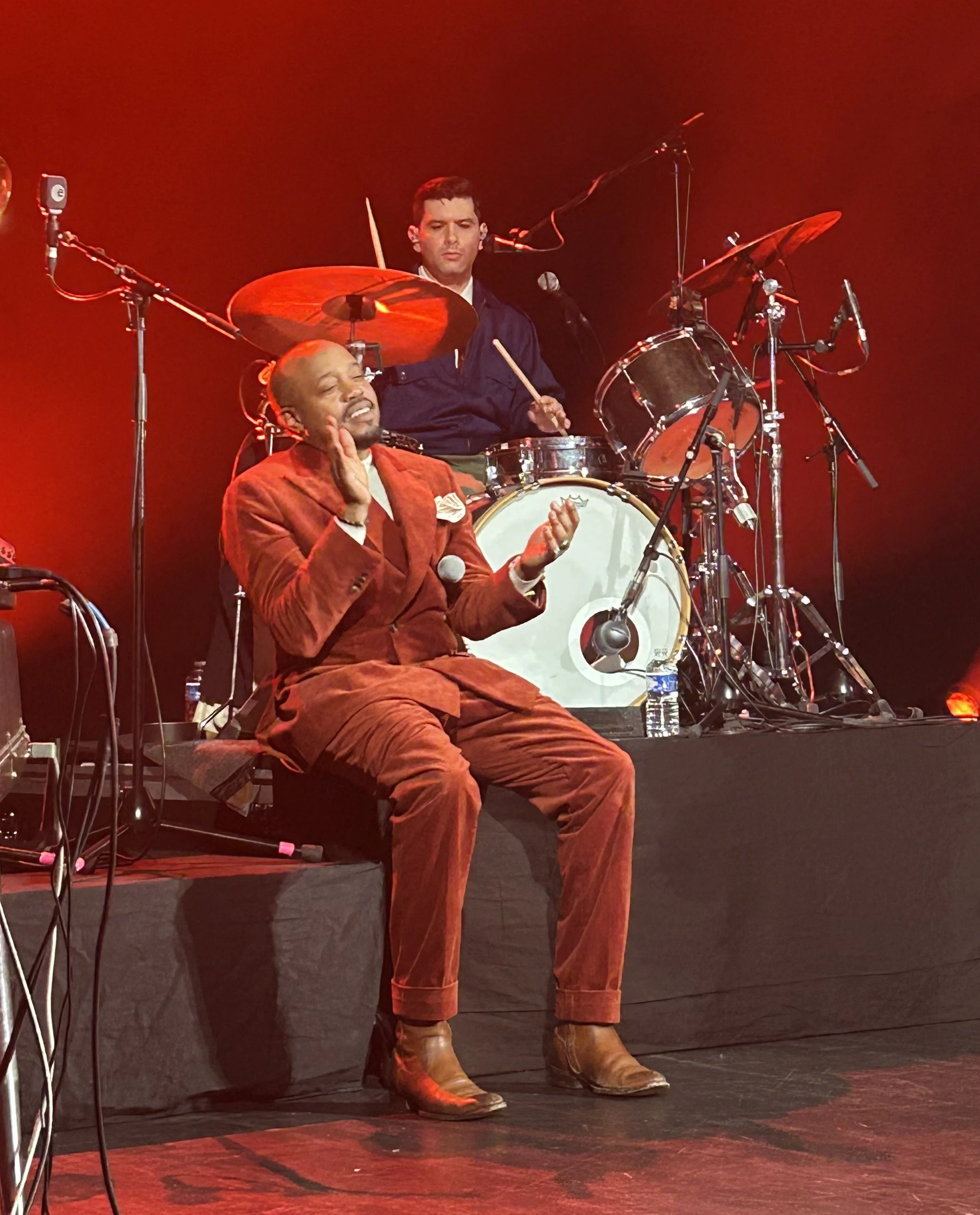 Durand Jones sitting in front of the drum kit clapping his hands while Aaron Frazier is playing the drums.