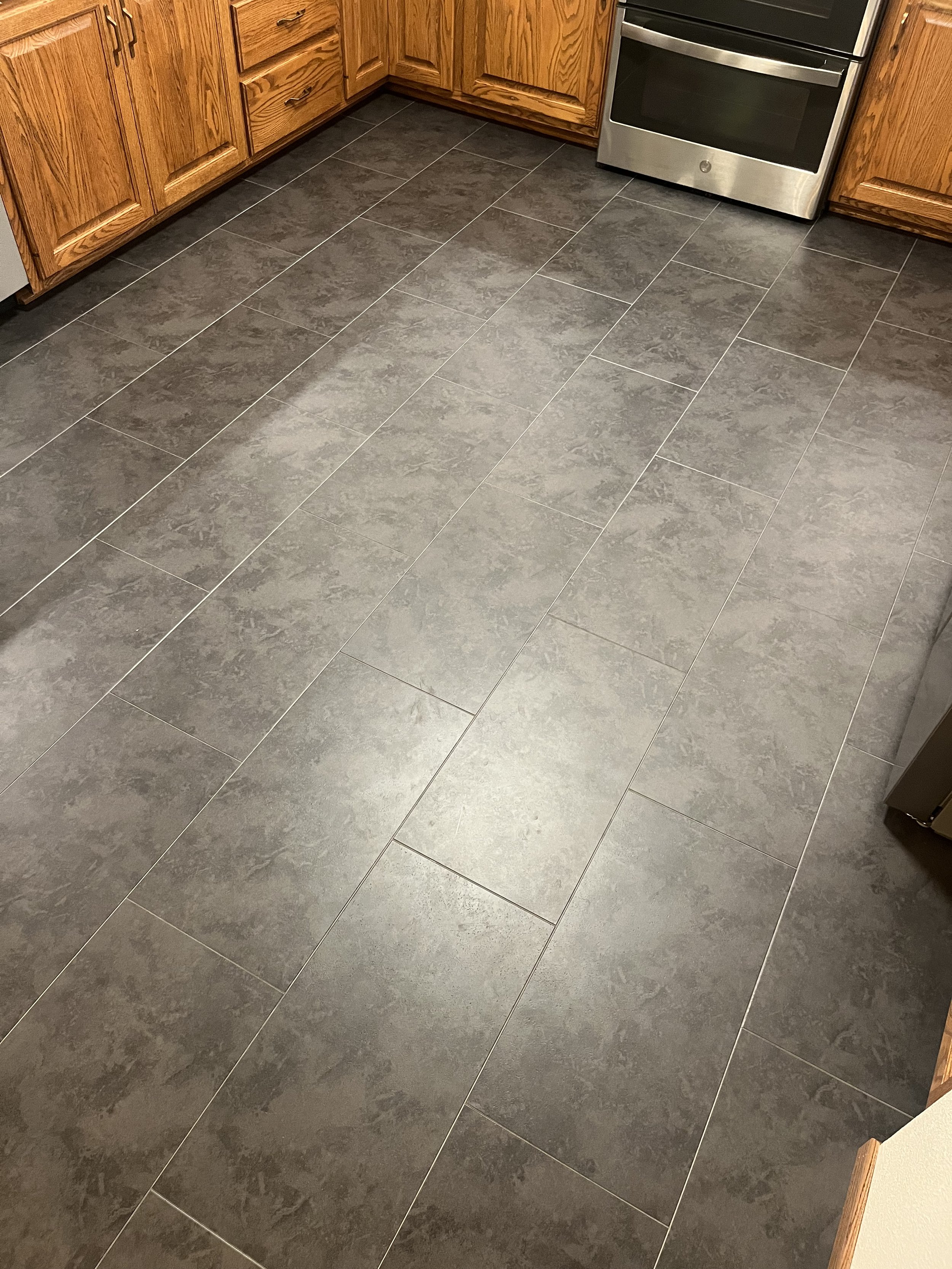 Modern kitchen with dark tile flooring, wooden cabinets, and stainless steel oven.