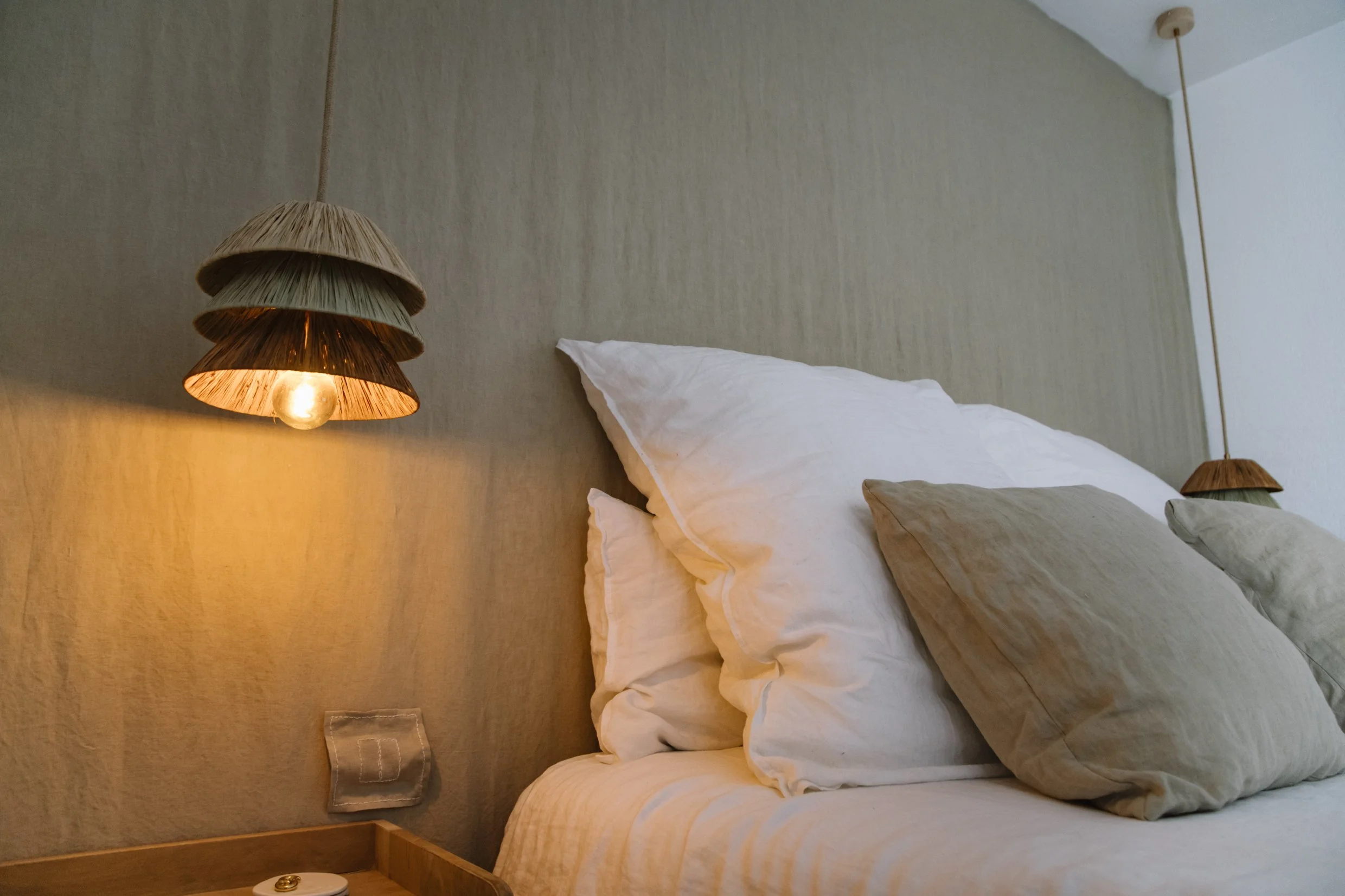 Lámpara artesanal de rafia Trina, iluminando un dormitorio con luz cálida y ambiente natural.