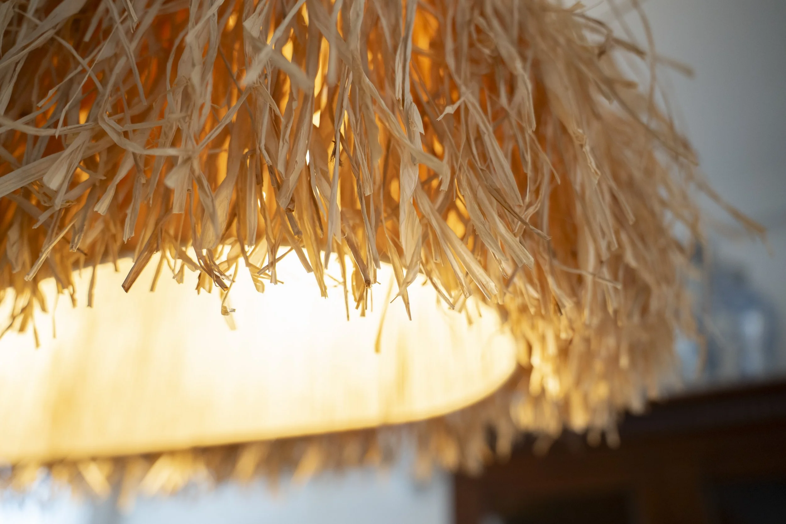 Detalle de una lámpara artesanal de rafia con flecos, filtrando una luz cálida y creando una atmósfera acogedora.