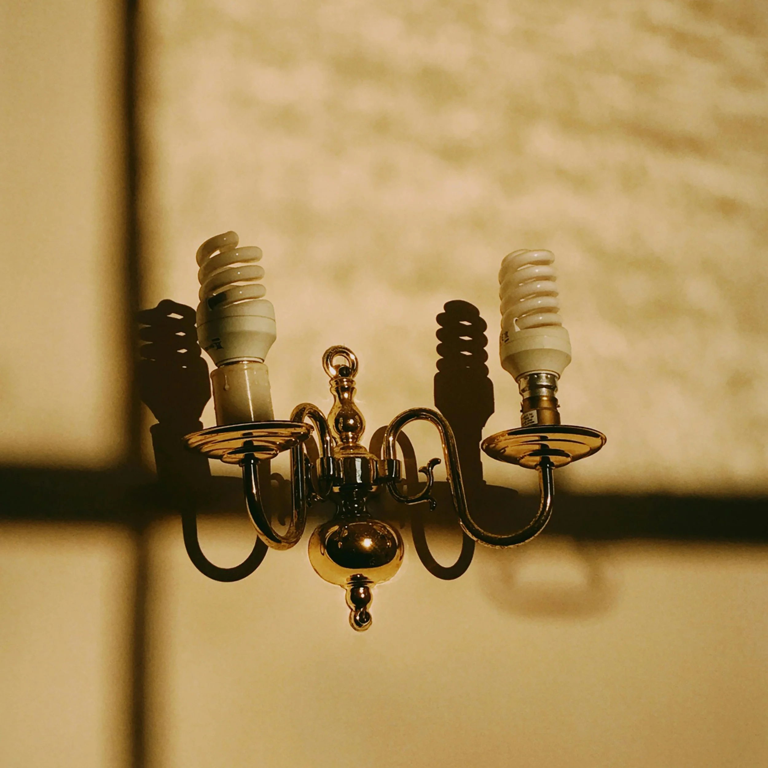 Lámpara de pared con bombillas visibles que proyectan sombras duras, ejemplo de iluminación poco confortable en interiores.