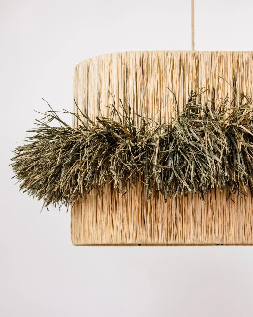 Lámpara de diseño con cuerpo alargado y tejida en rafia natural tintada en sus extremos a mano.