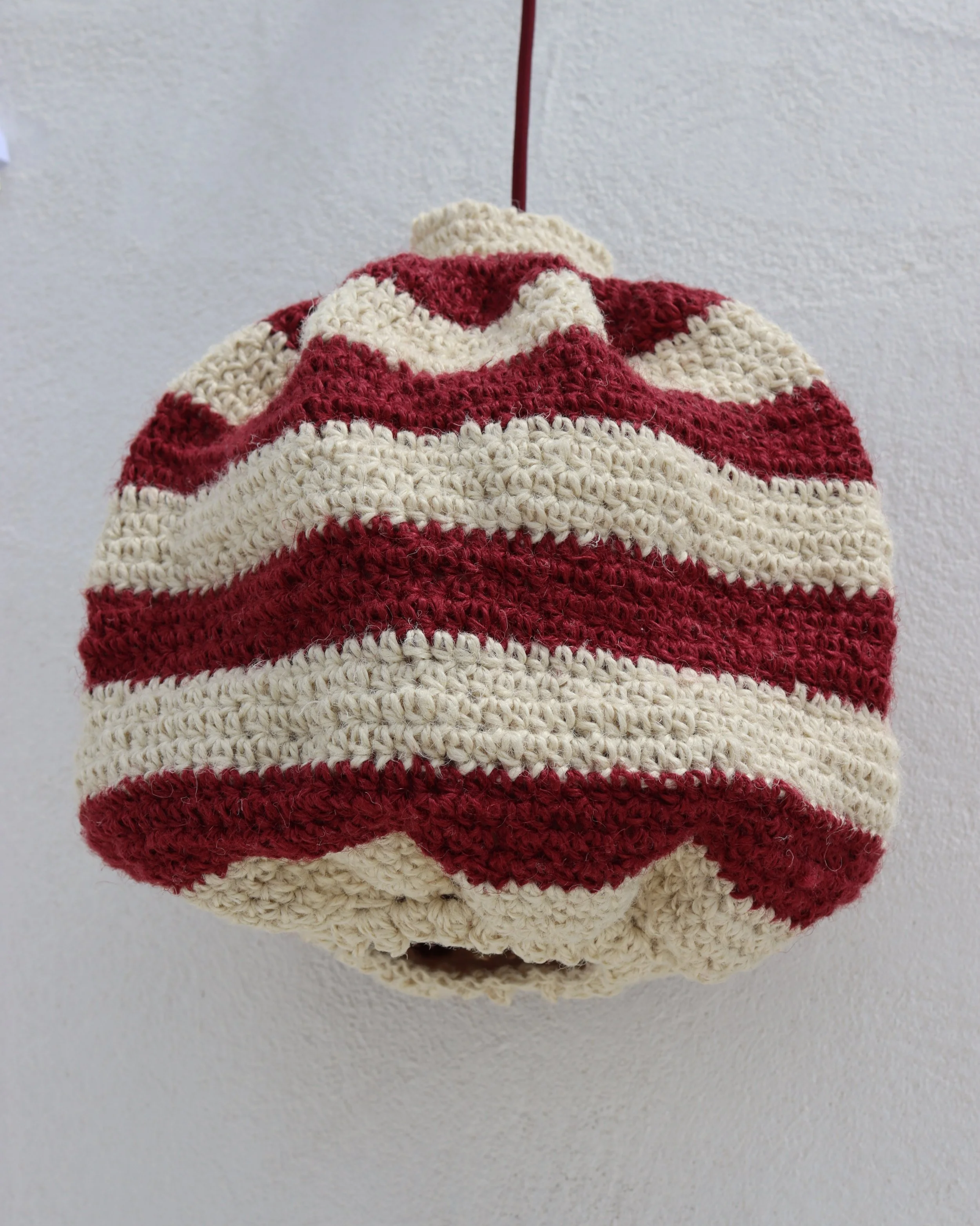 Abrigo de lana a rayas en colores rojo y crema colgado de un gancho en la pared.