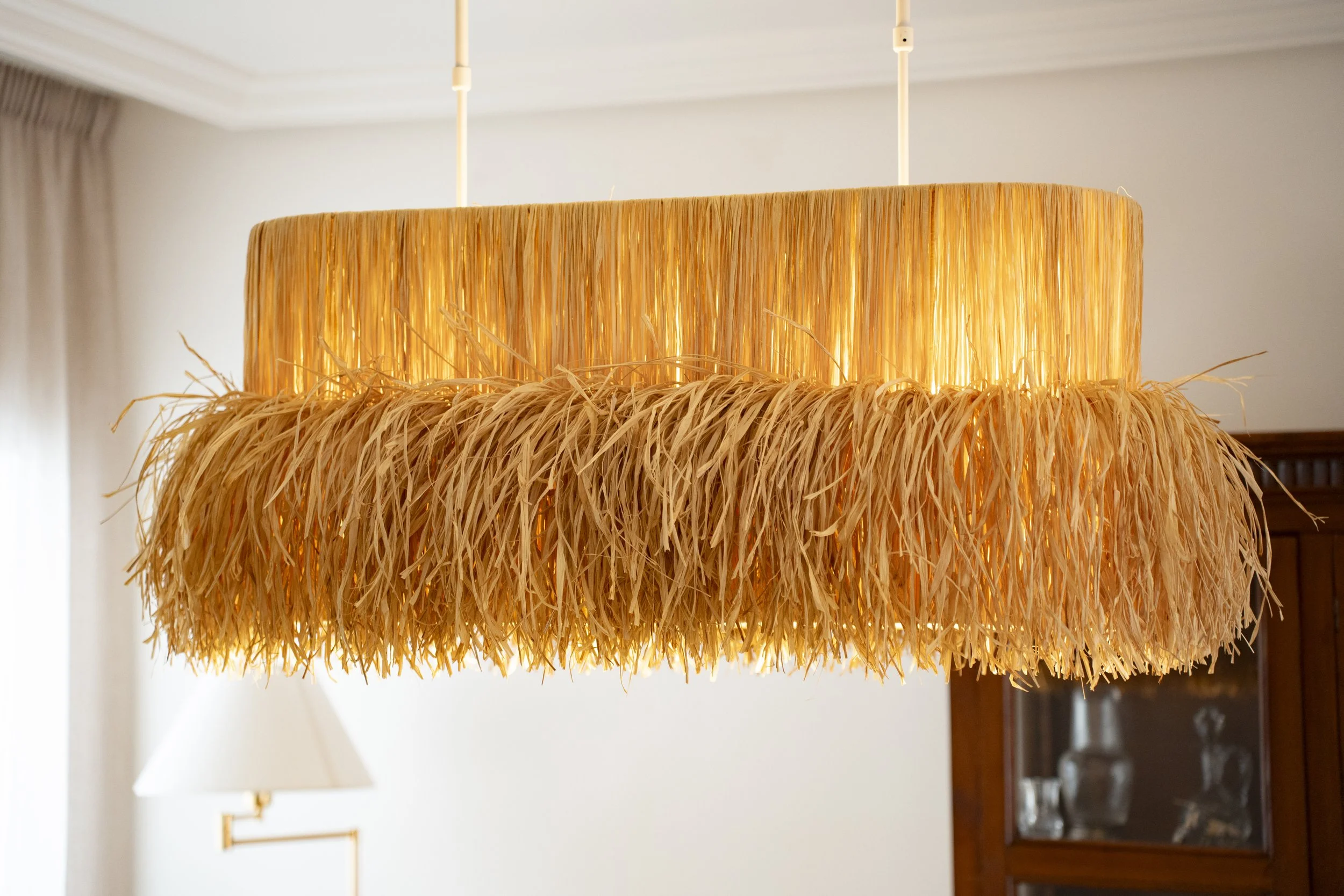 Lámpara artesanal de rafia proyectando una luz cálida y envolvente en un interior doméstico