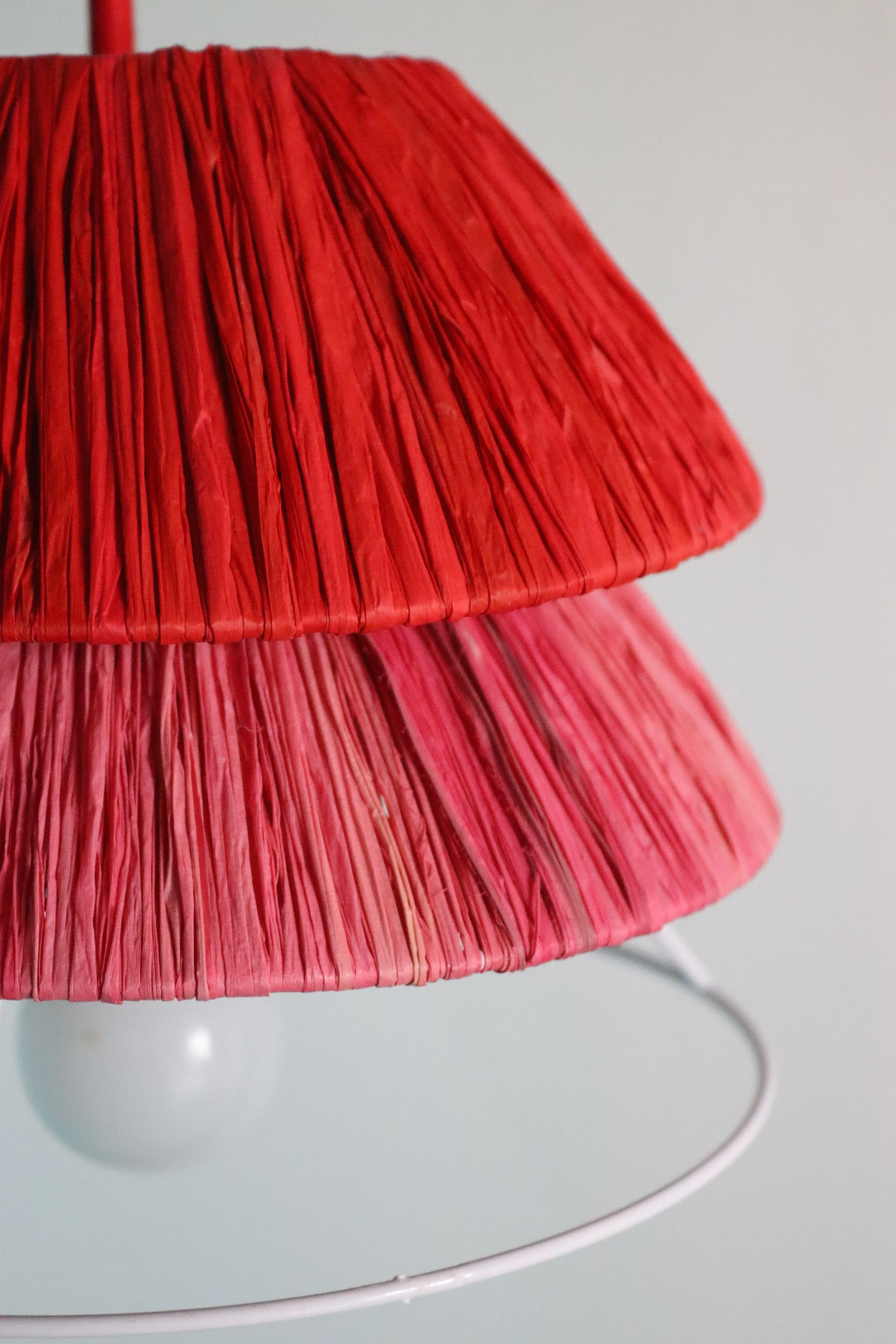 Detalle de rafia artesanal en lámpara TRINA, colores rojo y rosa tejidos a mano