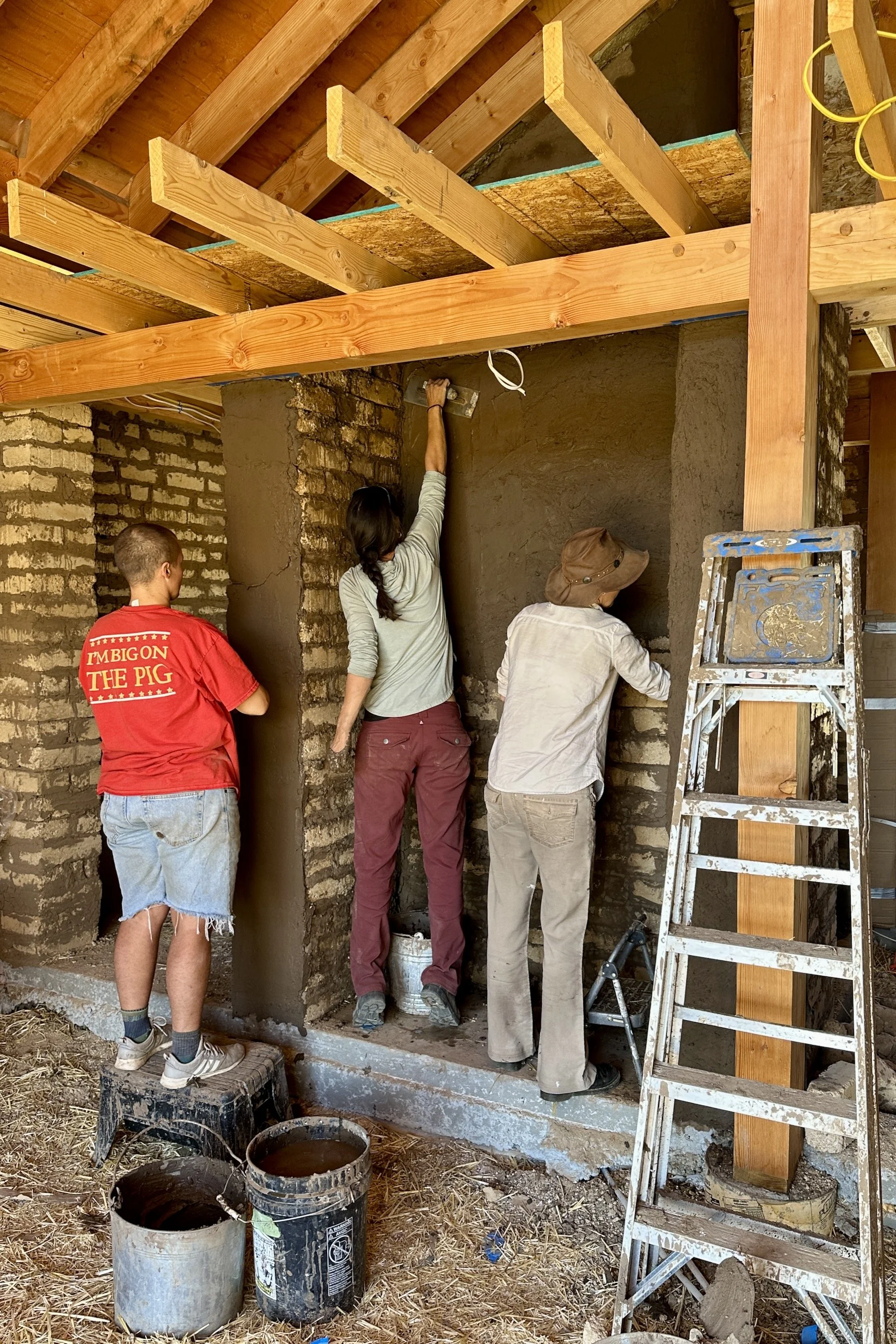 Students applying mud plaster to earthen wall