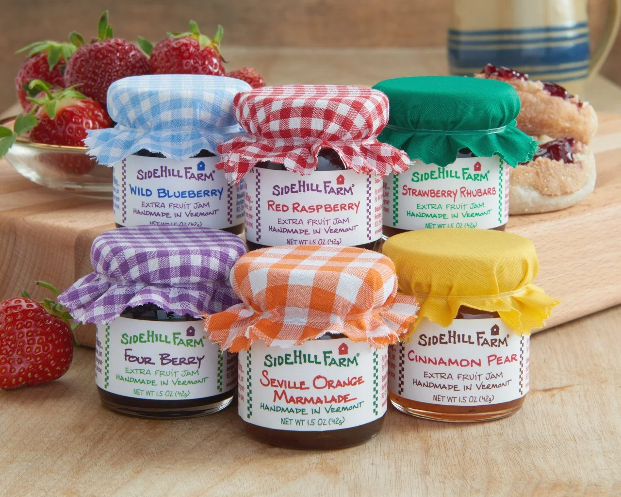A set of six jam jars. The lids are covered in gingham cloth.