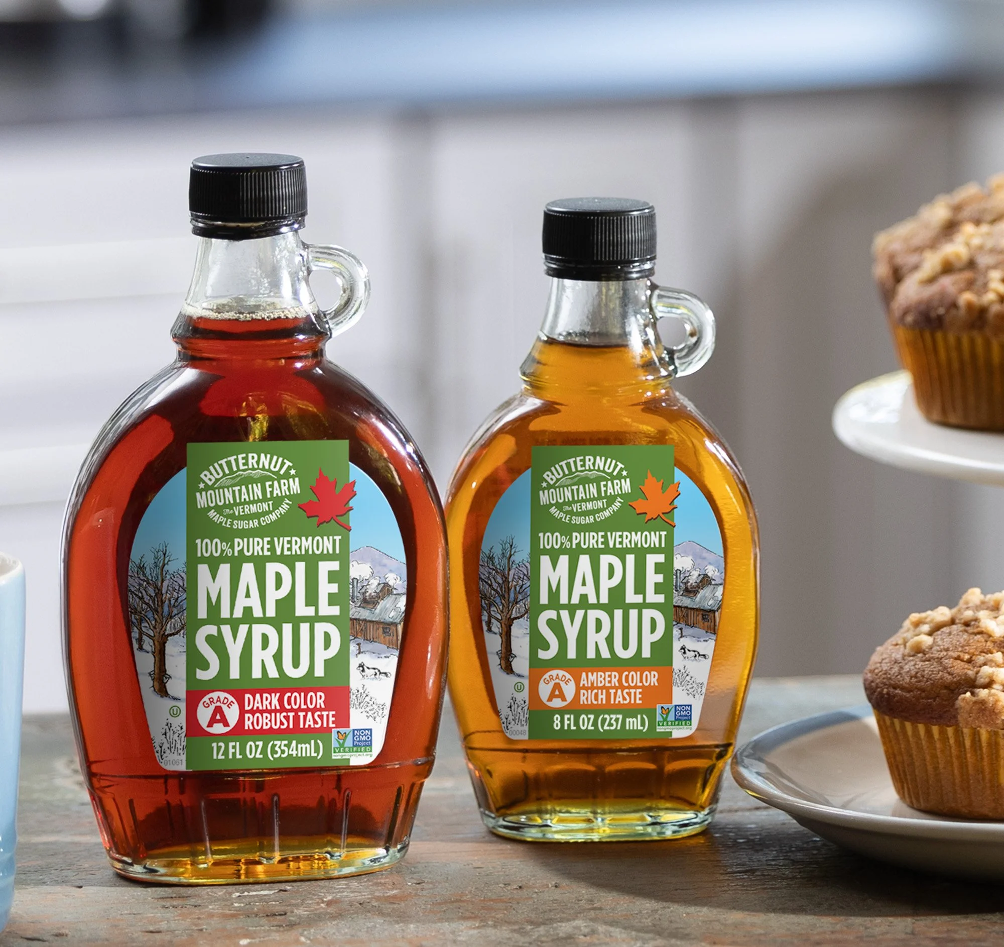 Grade A Dark Robust and Grade A Amber Rich glass bottles of pure maple syrup displayed next to muffins.